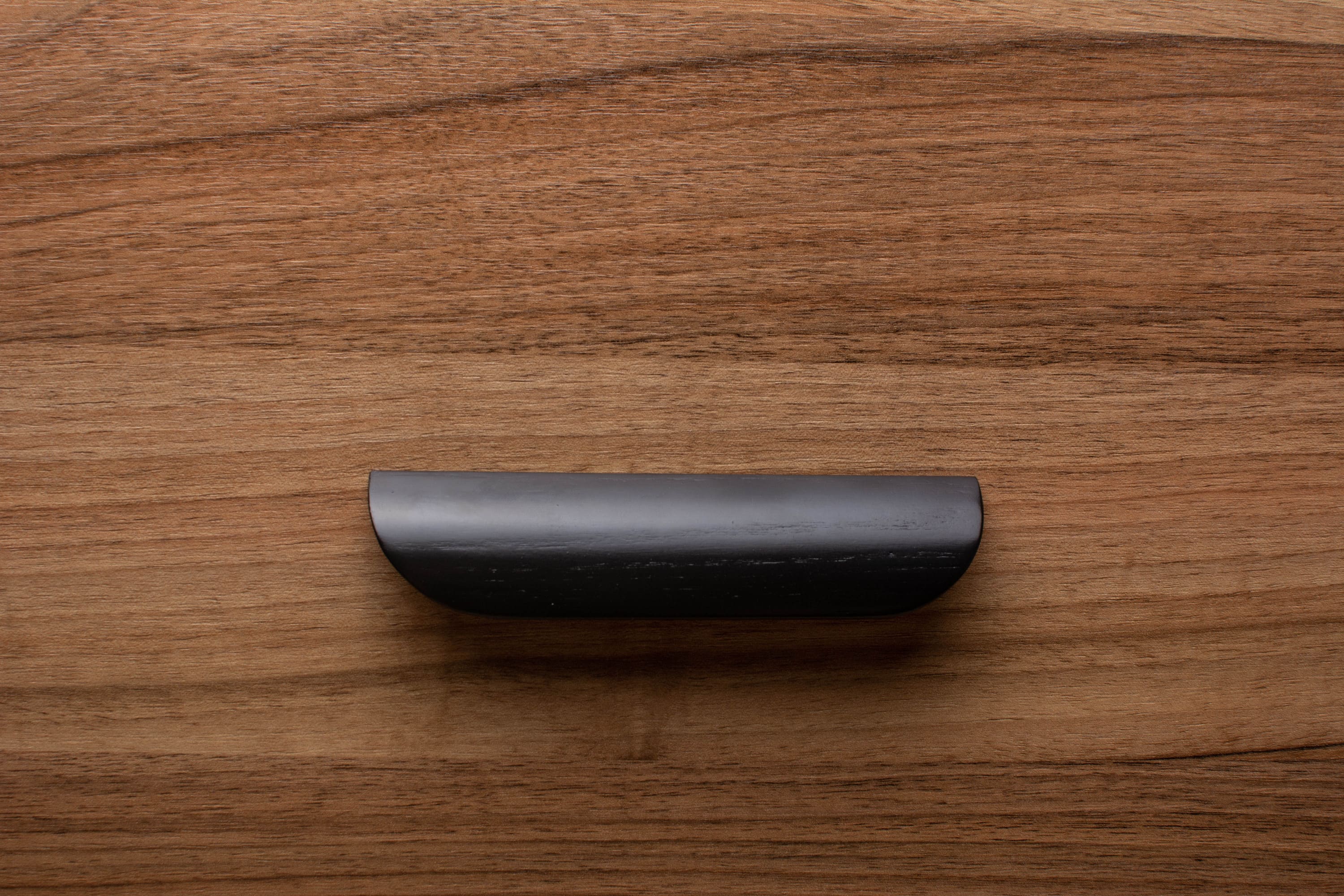 Black rounded handle on walnut drawer, ideal for modern minimalist furniture.