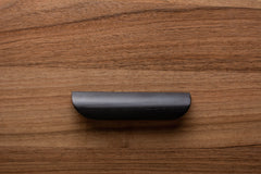 Black rounded handle on walnut drawer, ideal for modern minimalist furniture.