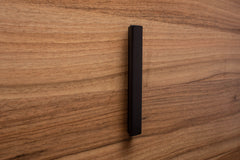 Black painted wooden handle attached to walnut drawer, showcasing modern elegance and clean lines.