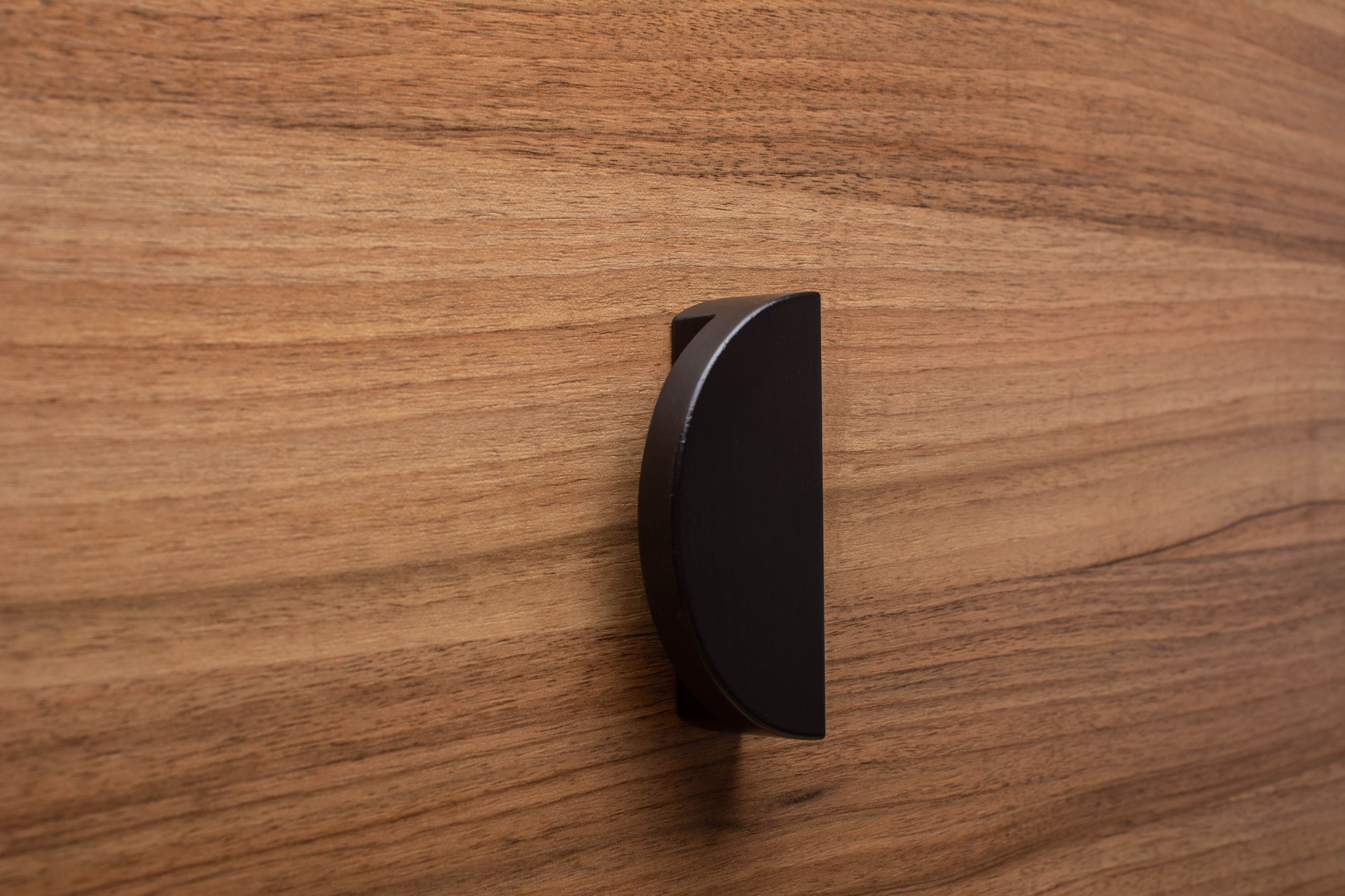 Modern black half moon handle on walnut drawer, ideal for sleek furniture design.