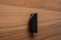 Modern black half moon handle on walnut drawer, ideal for sleek furniture design.