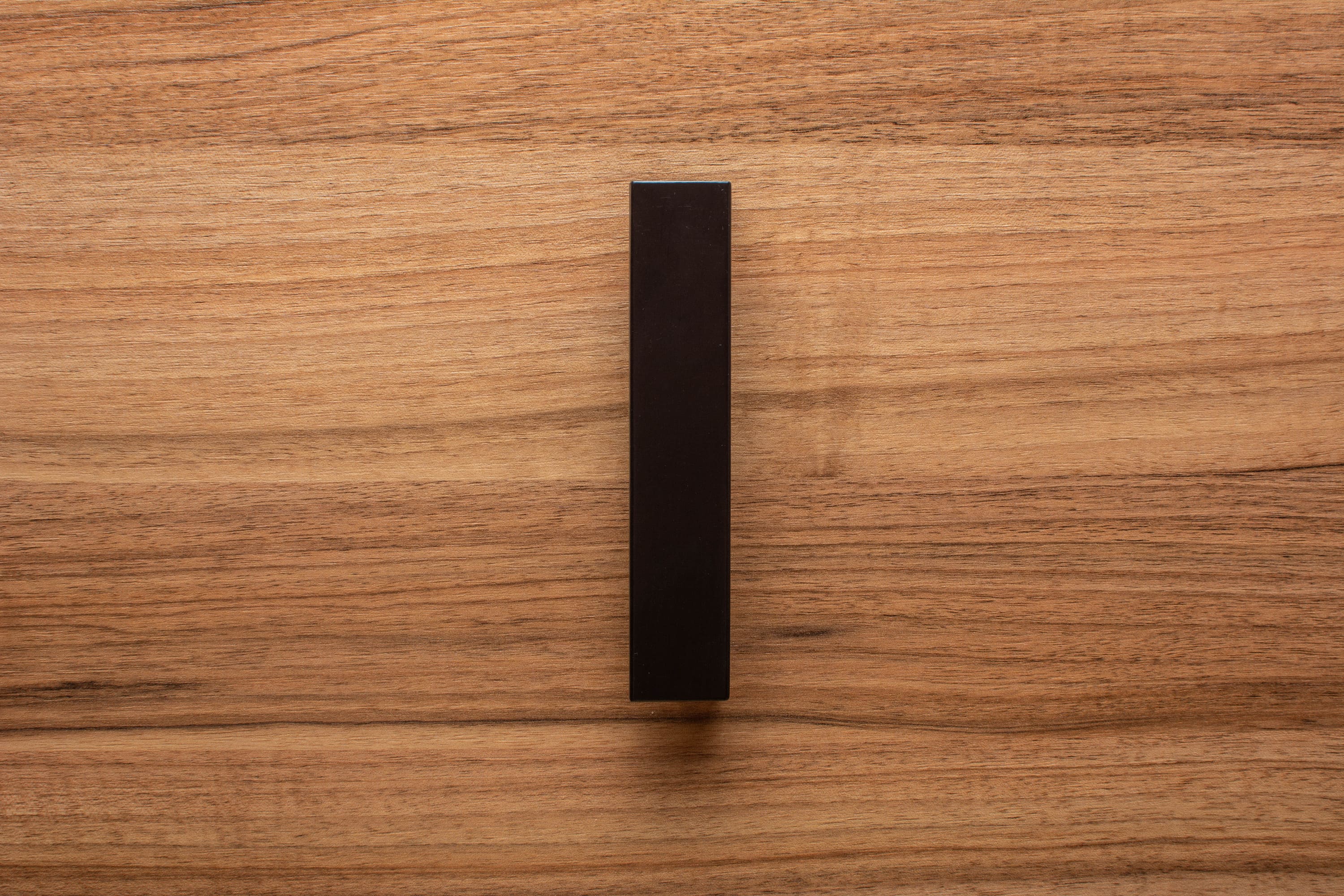 Modern L-form black handle affixed to walnut drawer, combining sharp lines with natural wood grain.