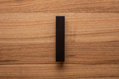 Modern L-form black handle affixed to walnut drawer, combining sharp lines with natural wood grain.
