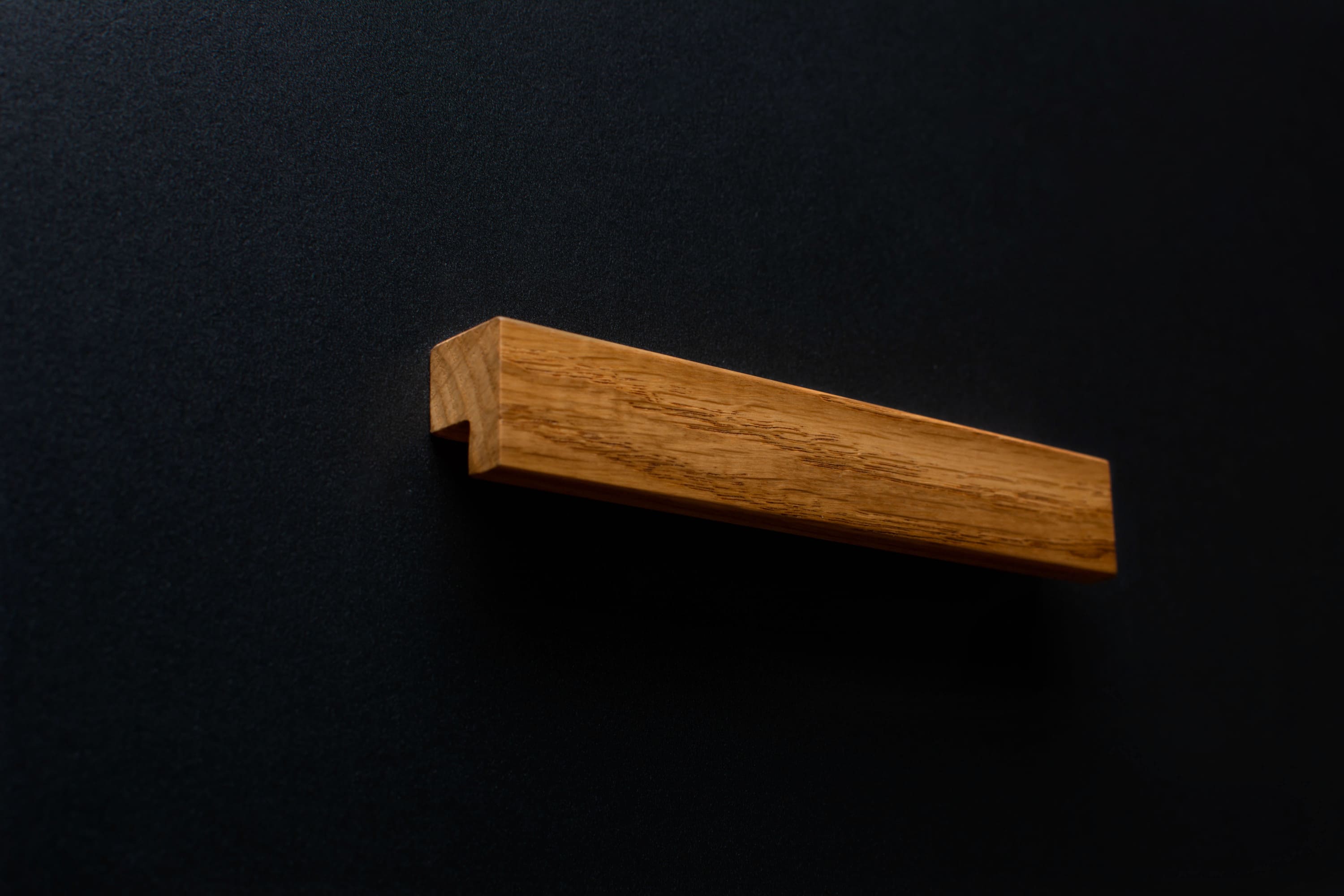 Close-up of Modern Oak Cabinet Handle on a black cabinet, showing detailed wood grain.