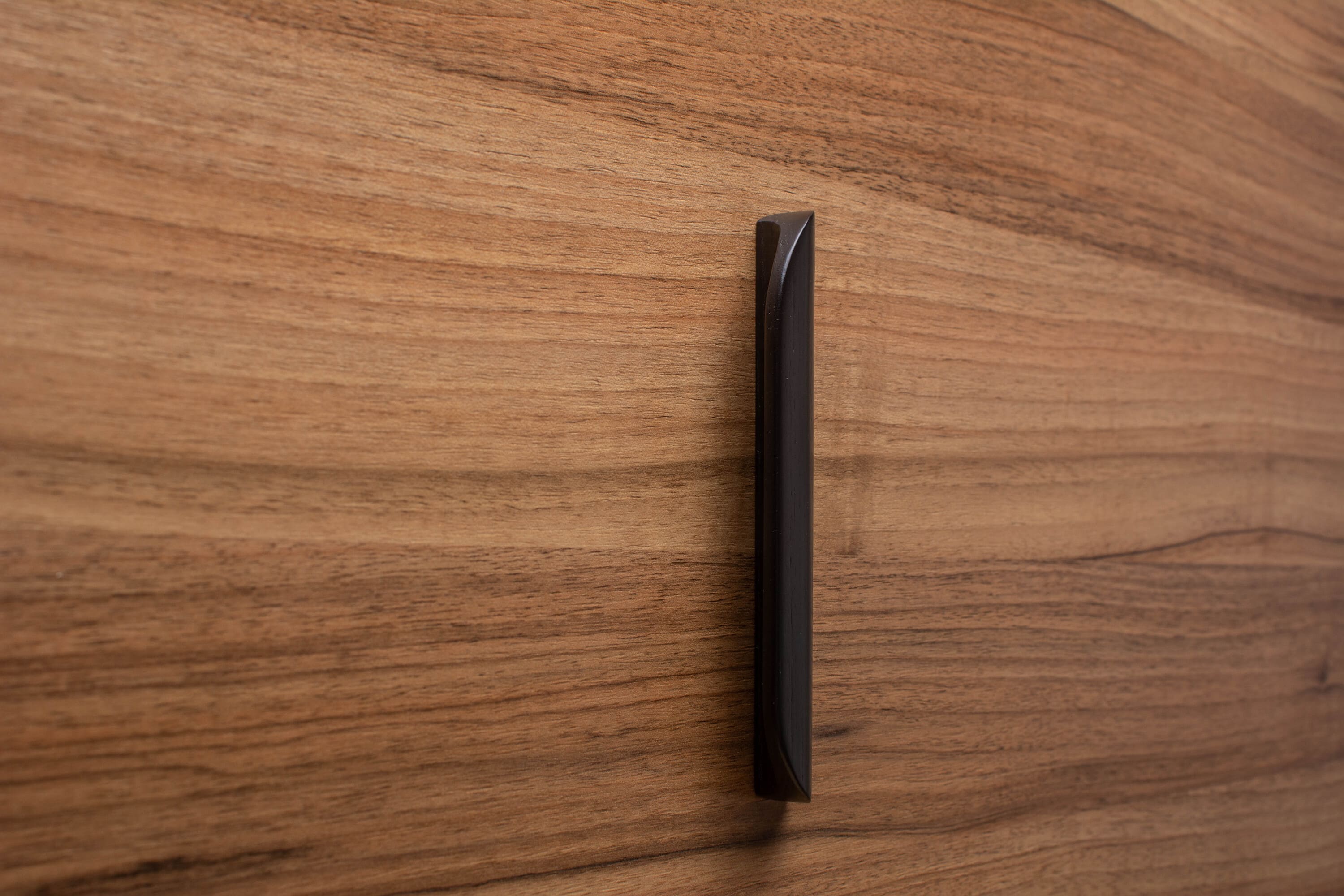 Modern rounded black wooden handle on walnut cabinet, enhancing sleek interiors.