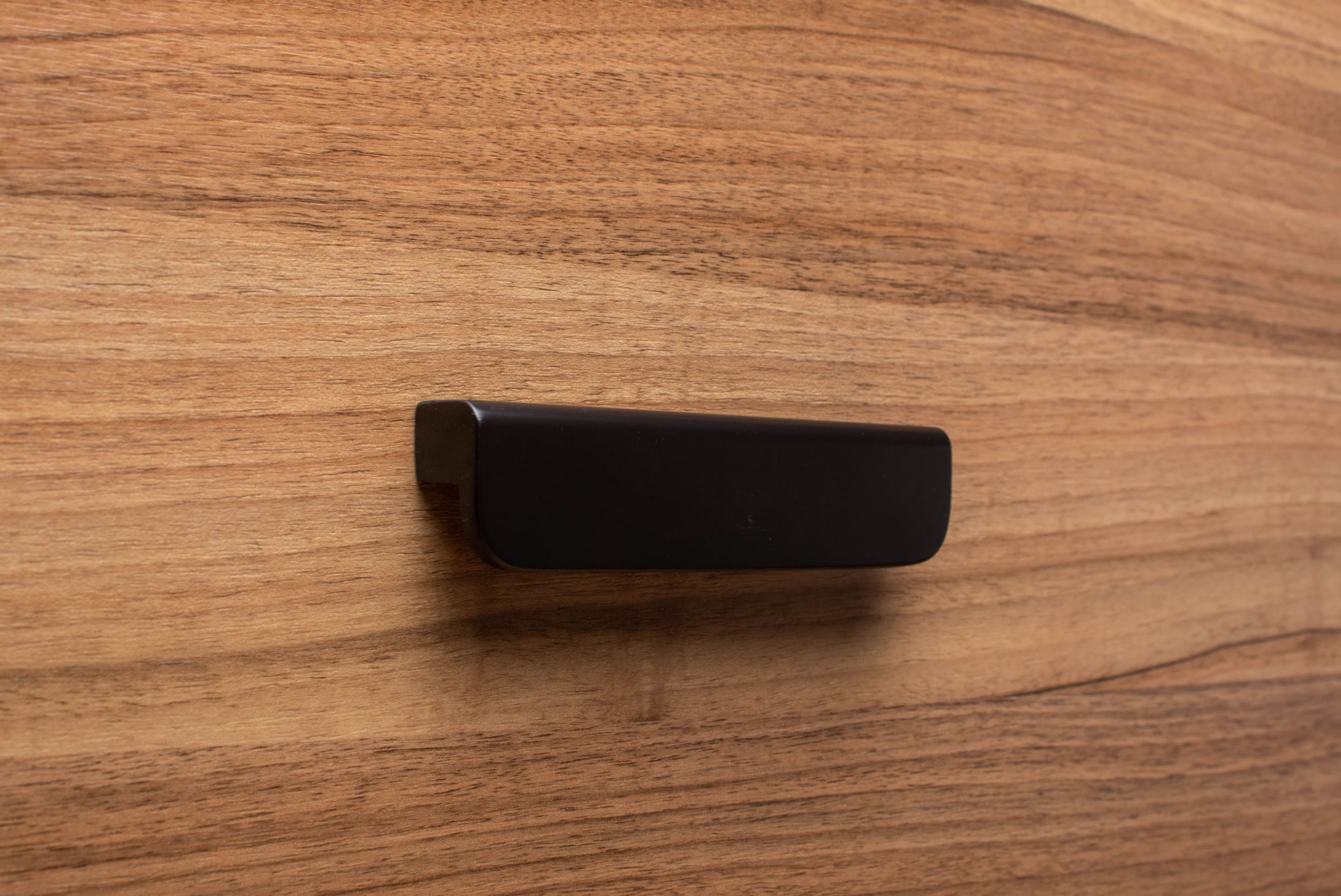 Wide grip rounded black handle mounted on walnut cabinet, showcasing modern design.