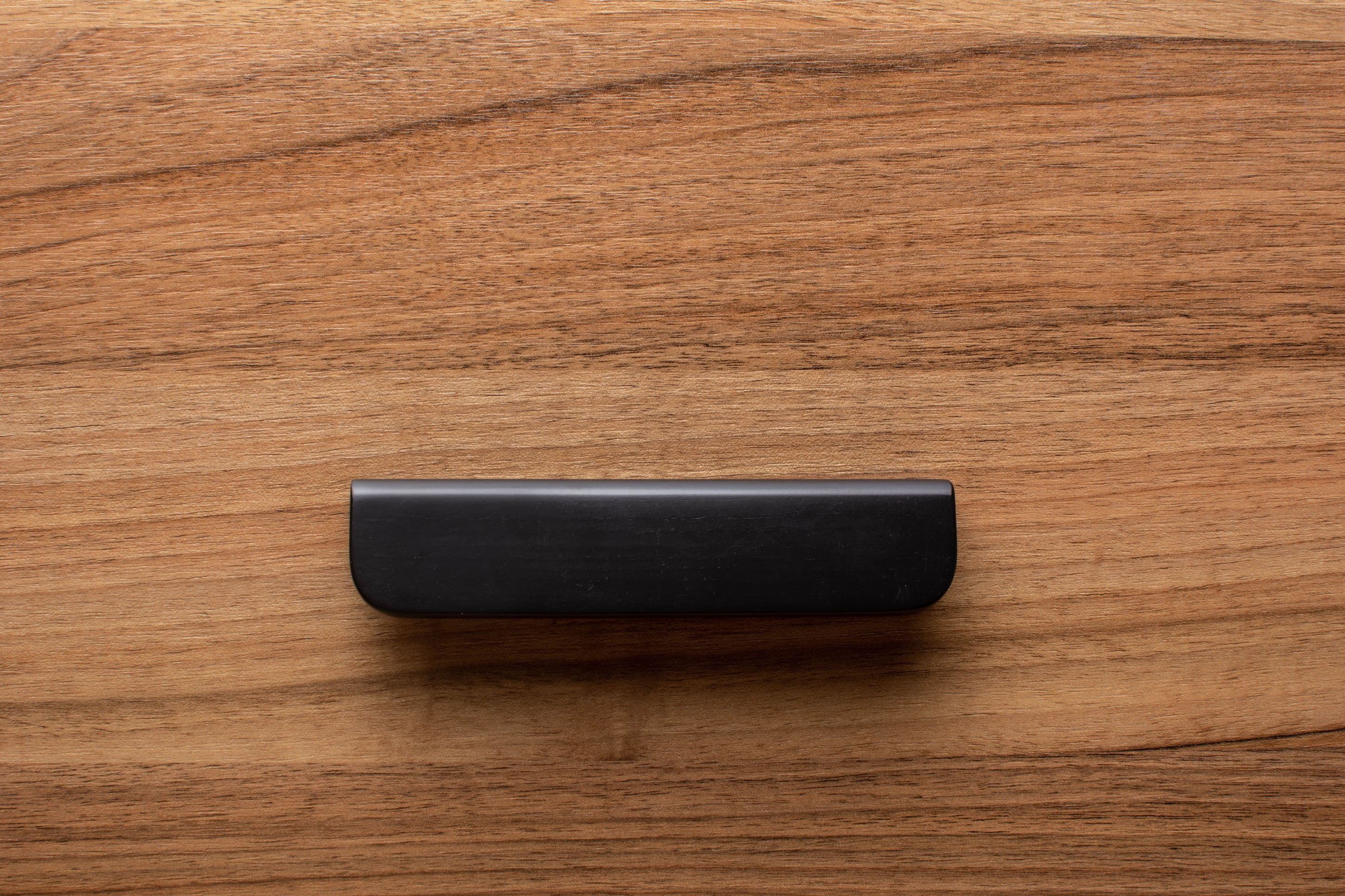 Modern rounded black cabinet handle with wide grip, elegantly contrasting walnut wood finish.