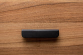 Modern rounded black cabinet handle with wide grip, elegantly contrasting walnut wood finish.