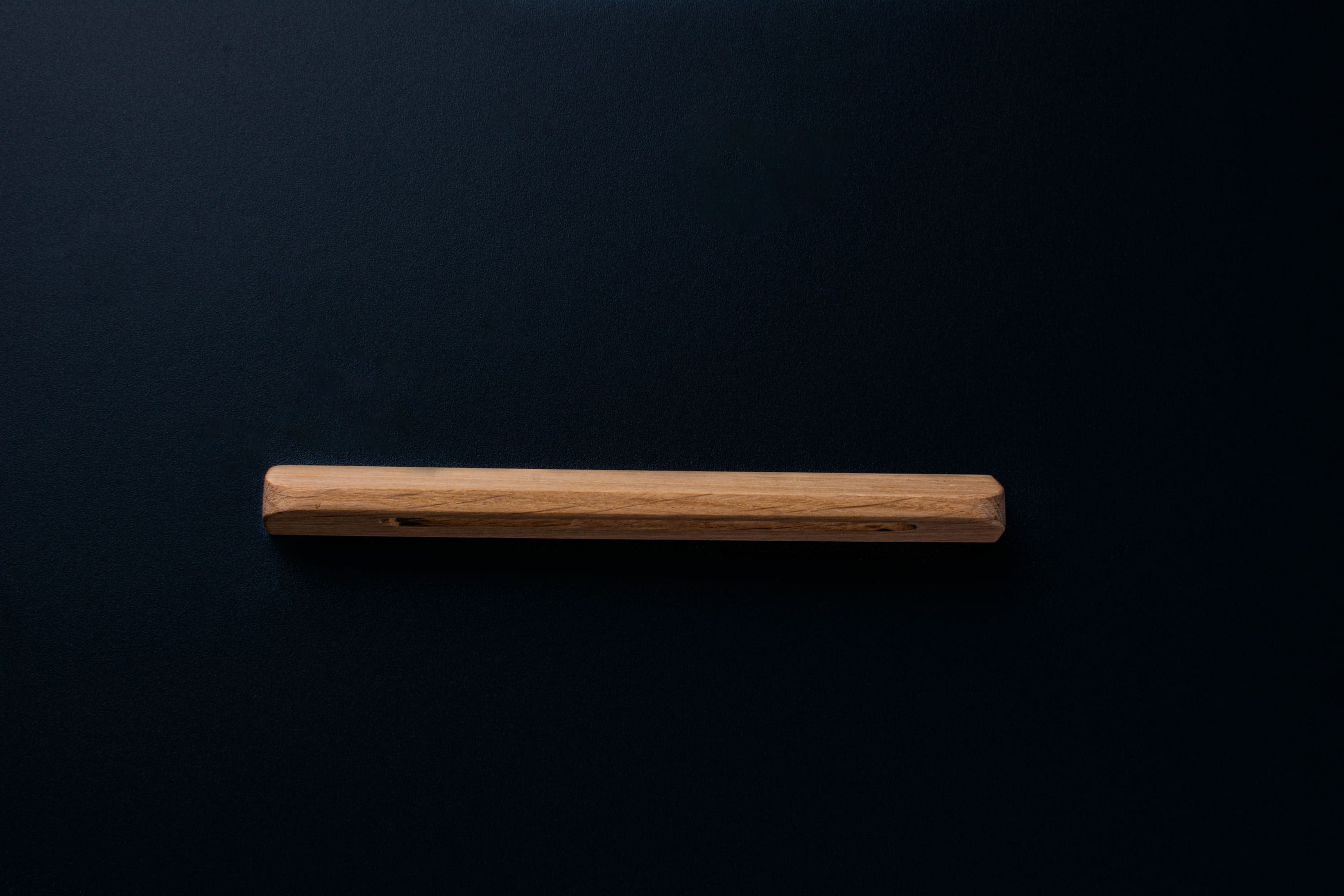 Custom-length unfinished oak handle centered on a matte black drawer