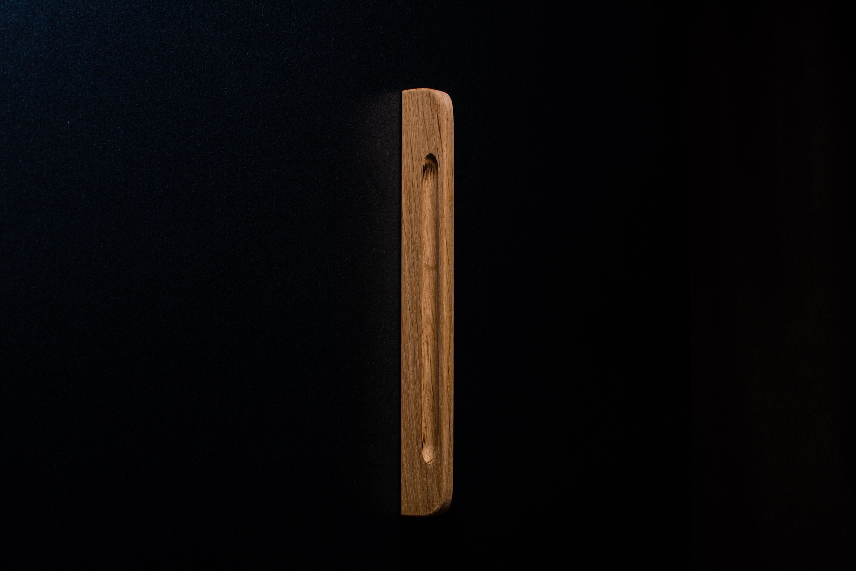 Close-up of light oak handle without finish, installed on dark cabinet