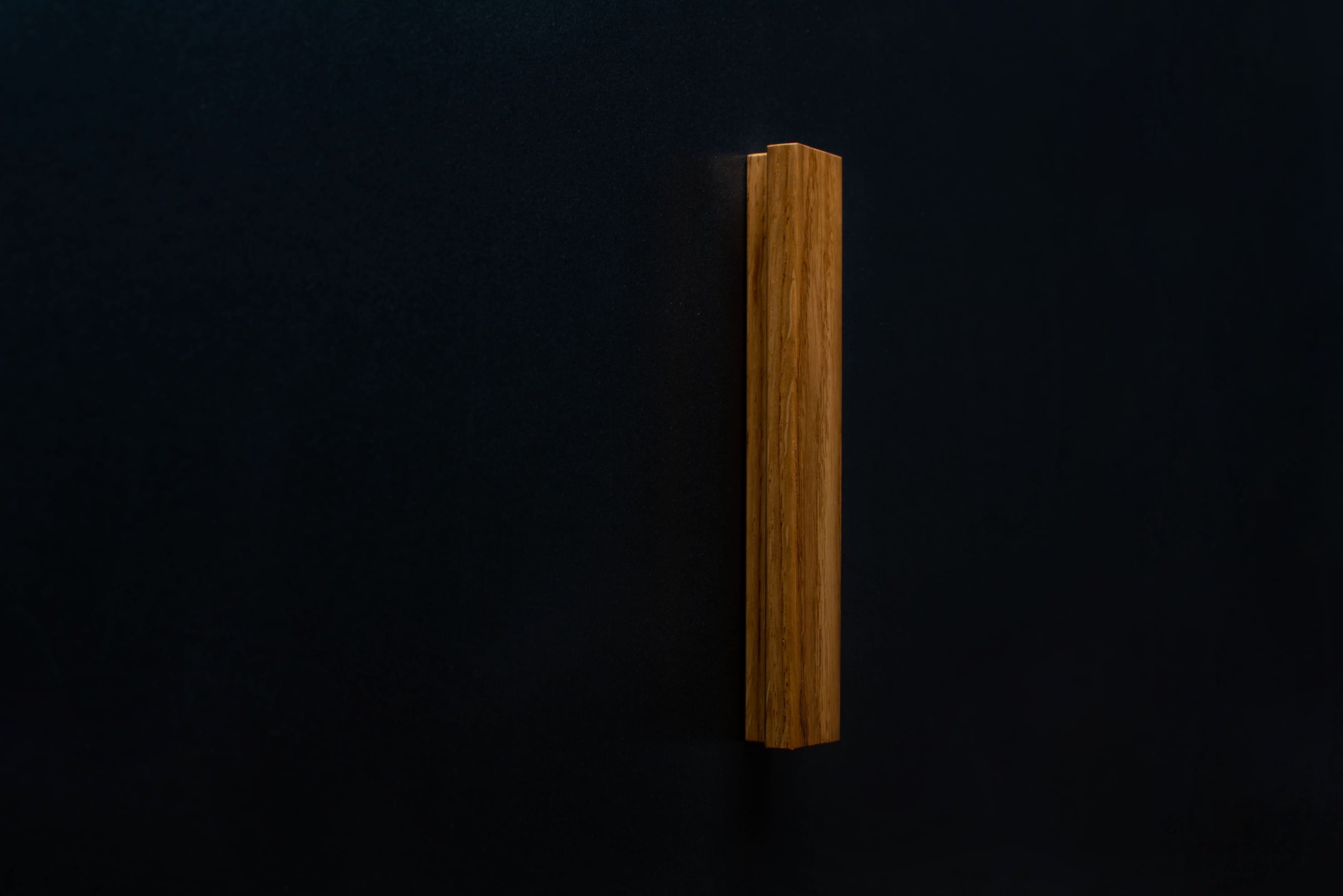 Top-down view of the Modern Oak Handle installed on a black cabinet, emphasizing the sleek contrast between wood and black surface.