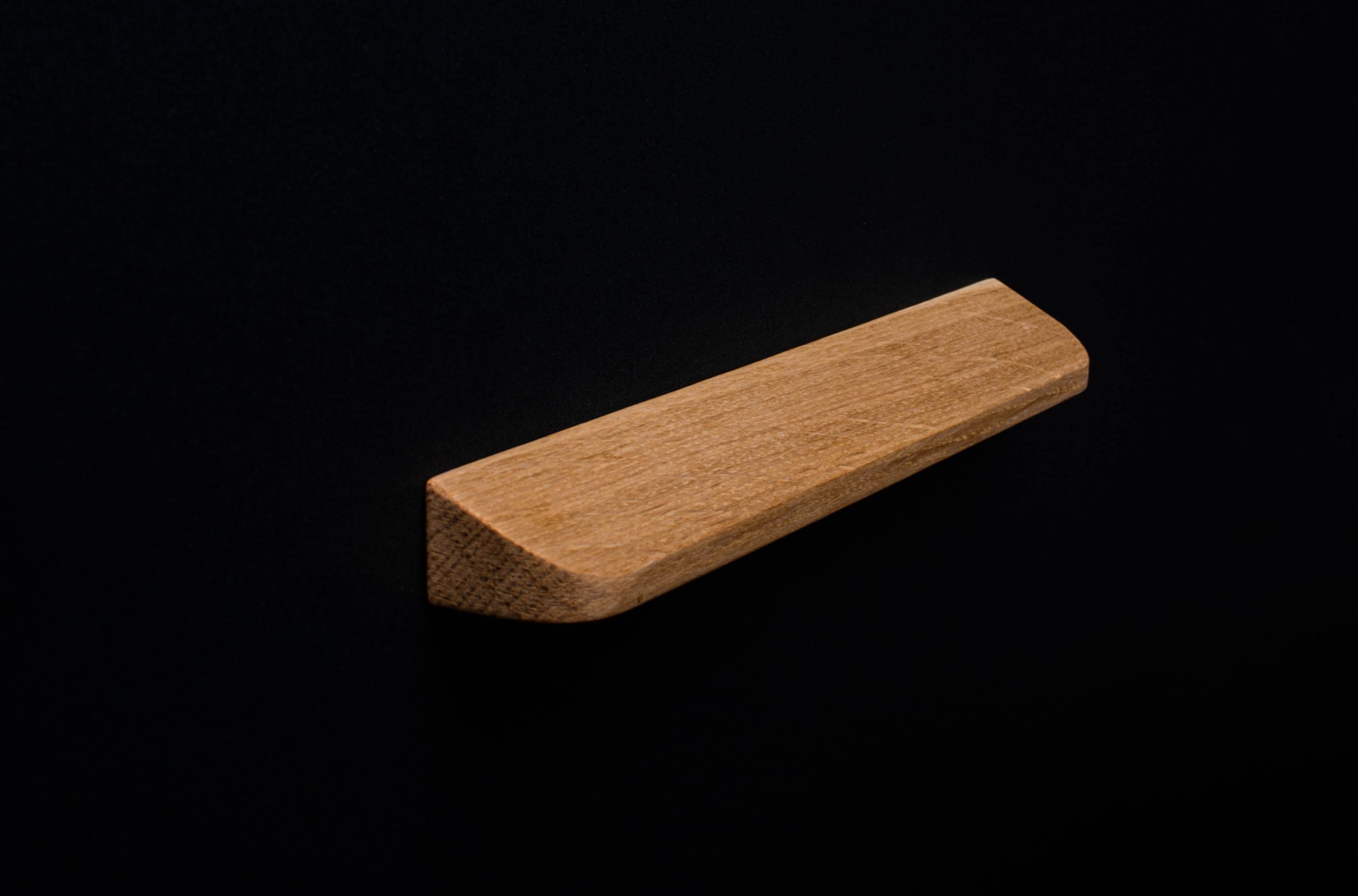 Unfinished oak cabinet pull installed on black furniture, natural wood grain visible