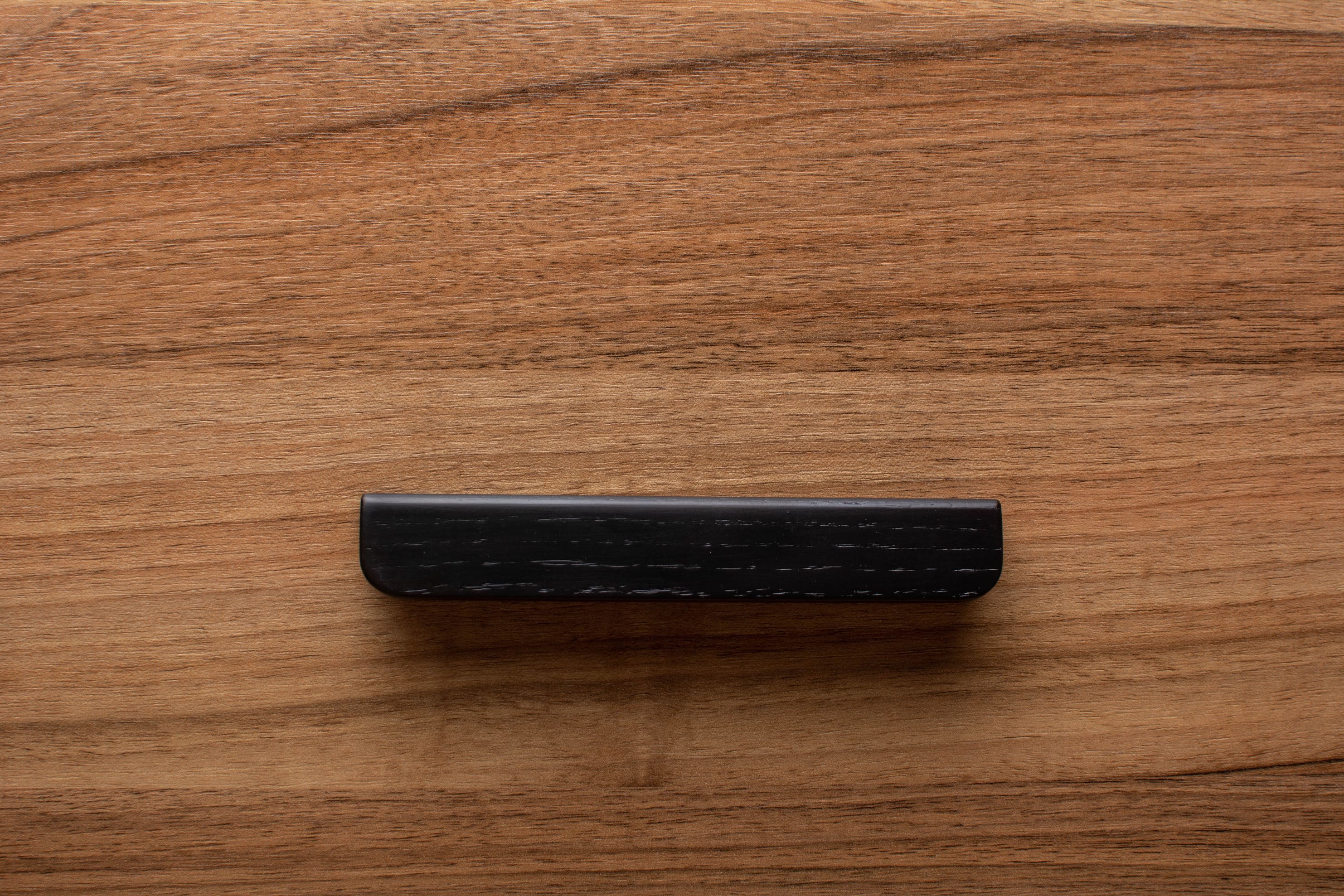 Black rounded cabinet handle on walnut drawer, perfect for minimalist modern interiors.