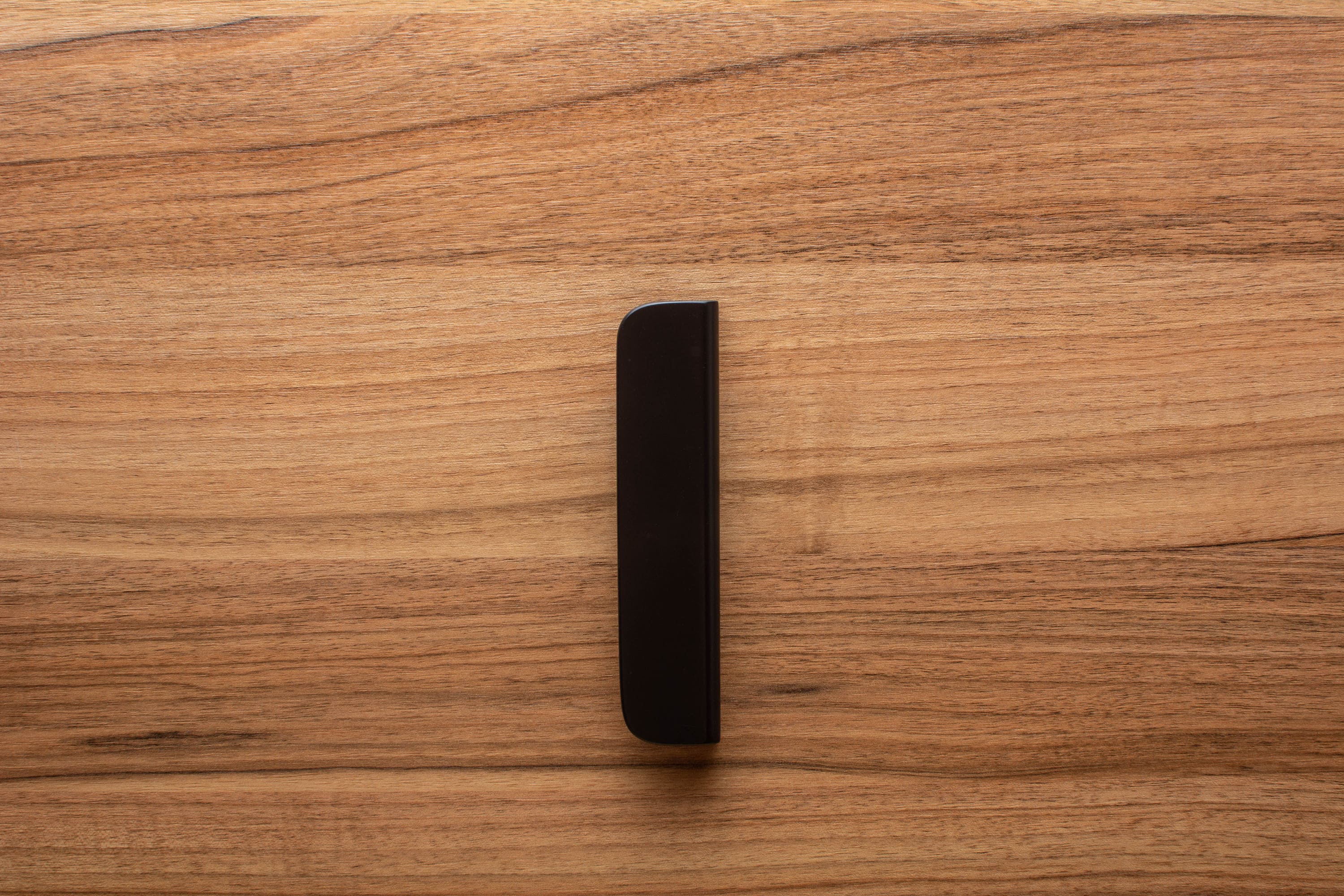 Rounded black cabinet handle with wide grip, accentuating the rich walnut wood grain.