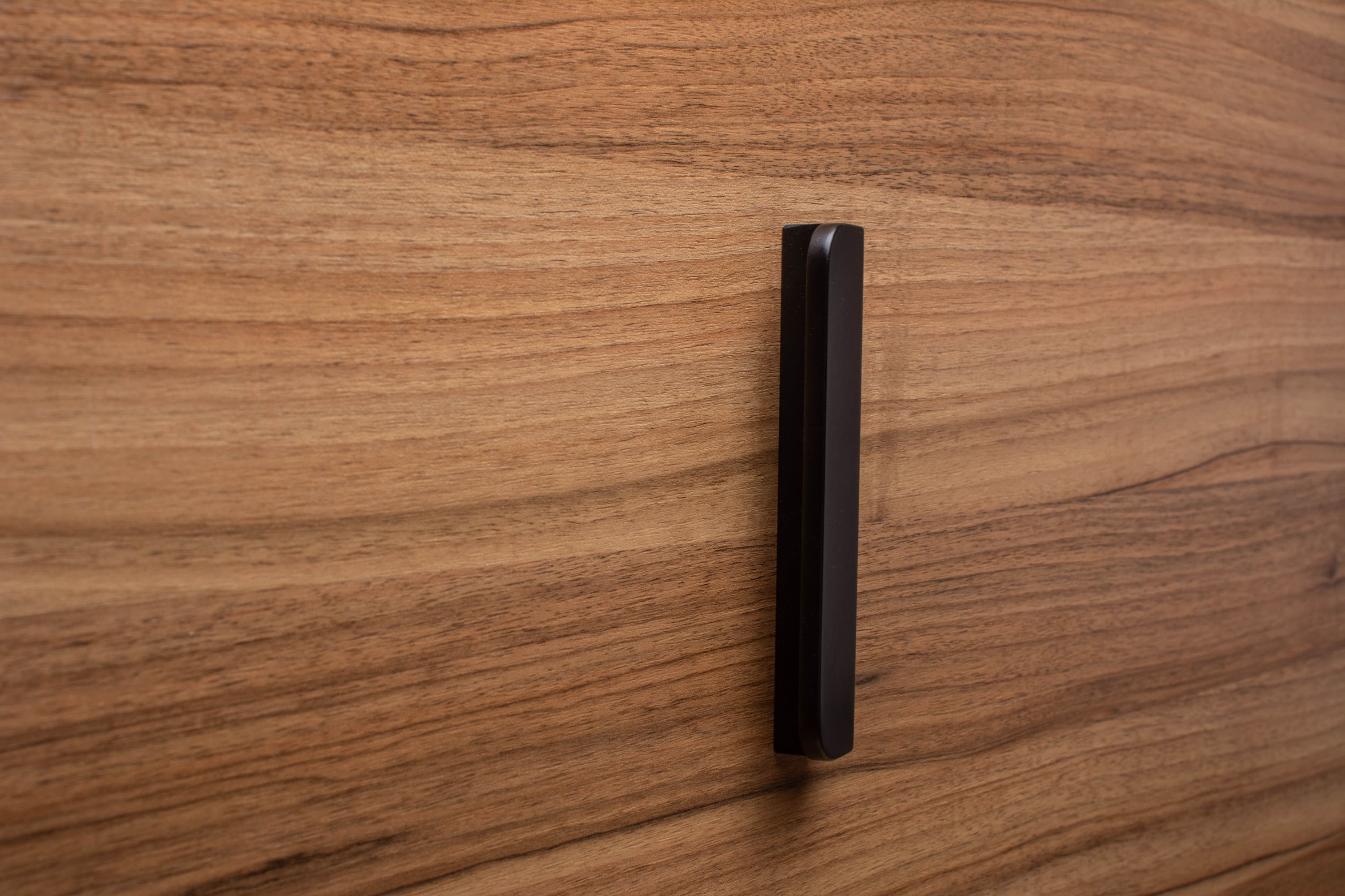 Rounded black cabinet handle with wide grip on walnut, highlighting craftsmanship and modern design.