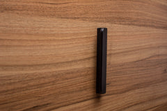 Rounded black cabinet handle with wide grip on walnut, highlighting craftsmanship and modern design.