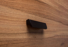 Rounded black handle with wide grip attached to walnut cabinet, emphasizing sleek design and practicality.