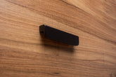 Rounded black cabinet handle with wide grip on walnut wood, offering a sleek contrast.