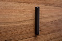 Sleek black rounded handle on walnut cabinet, a minimalist detail for modern furniture.