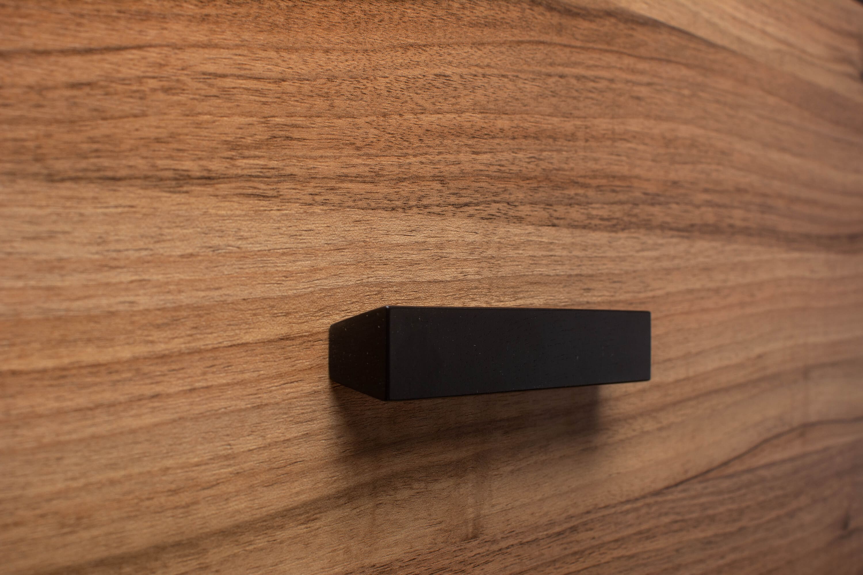 Unique trapezoidal black wooden handle on walnut cabinet, offering a sleek, modern touch.