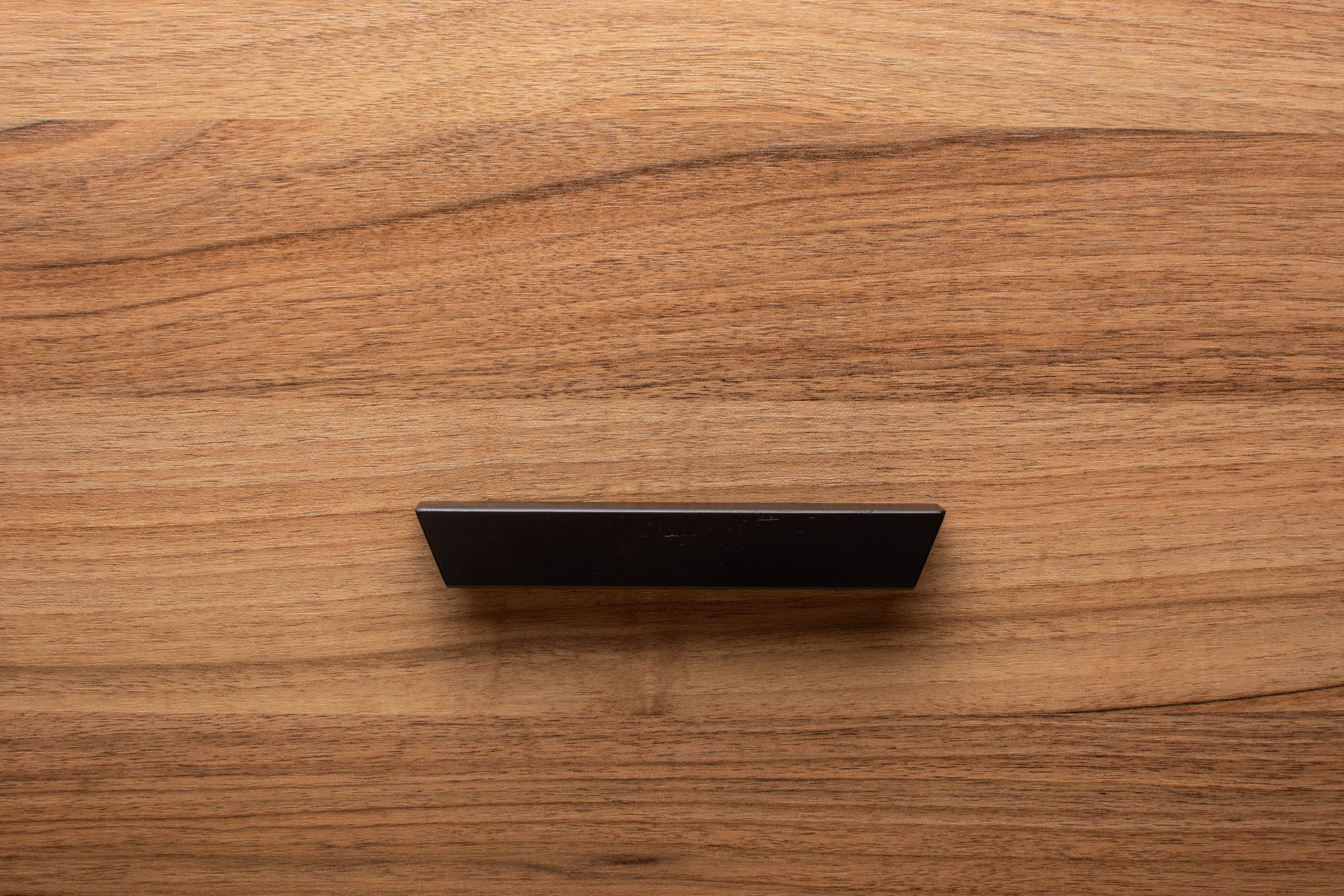 Stylish black cabinet handle on walnut drawer, offering a contemporary touch to the wood grain.