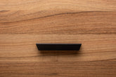 Stylish black cabinet handle on walnut drawer, offering a contemporary touch to the wood grain.