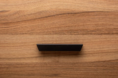 Stylish black cabinet handle on walnut drawer, offering a contemporary touch to the wood grain.