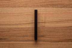 Top-down view of black wooden cabinet handle on walnut door, highlighting the modern look.