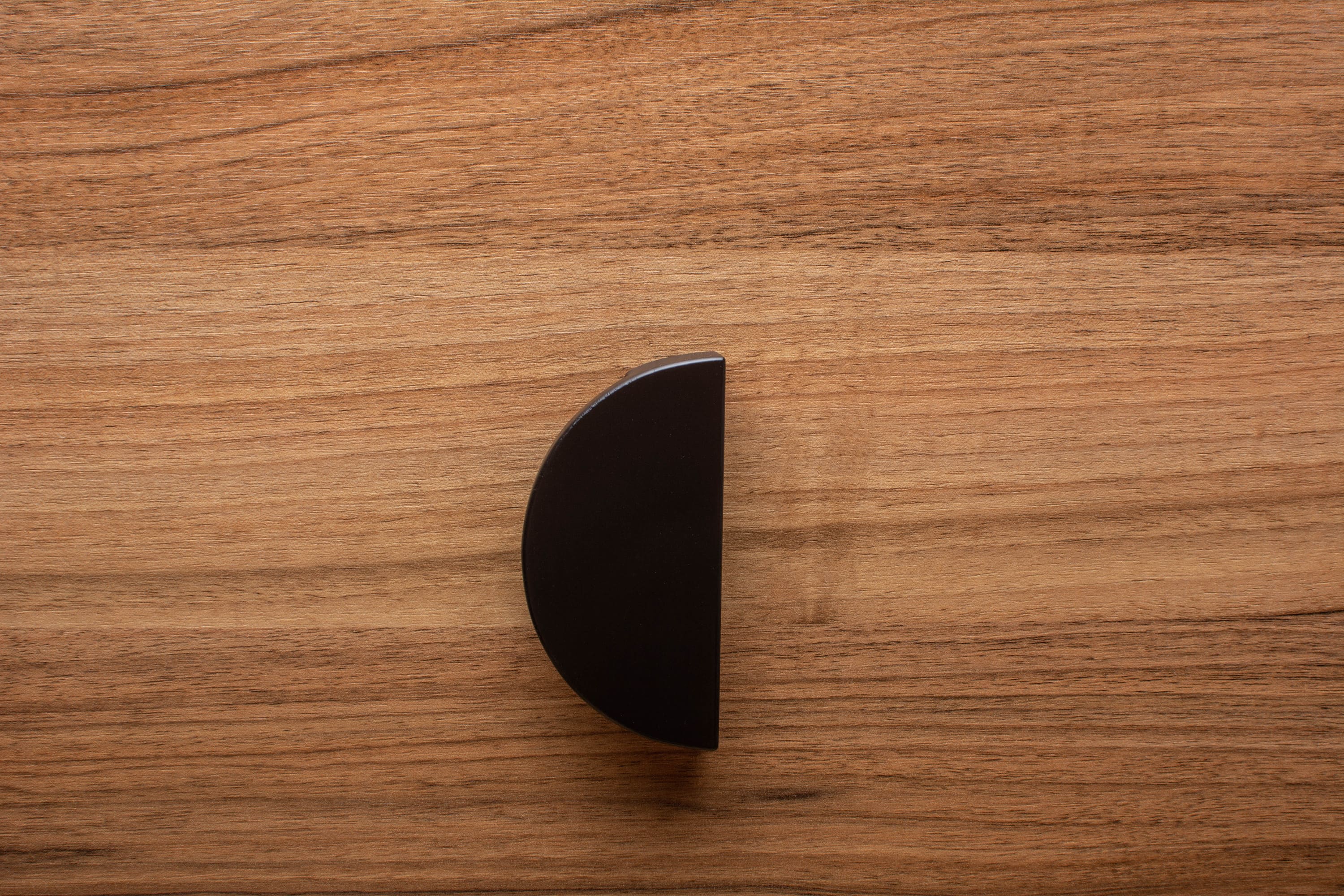 Stylish half moon black handle on walnut cabinet, combining modern aesthetics with functionality.
