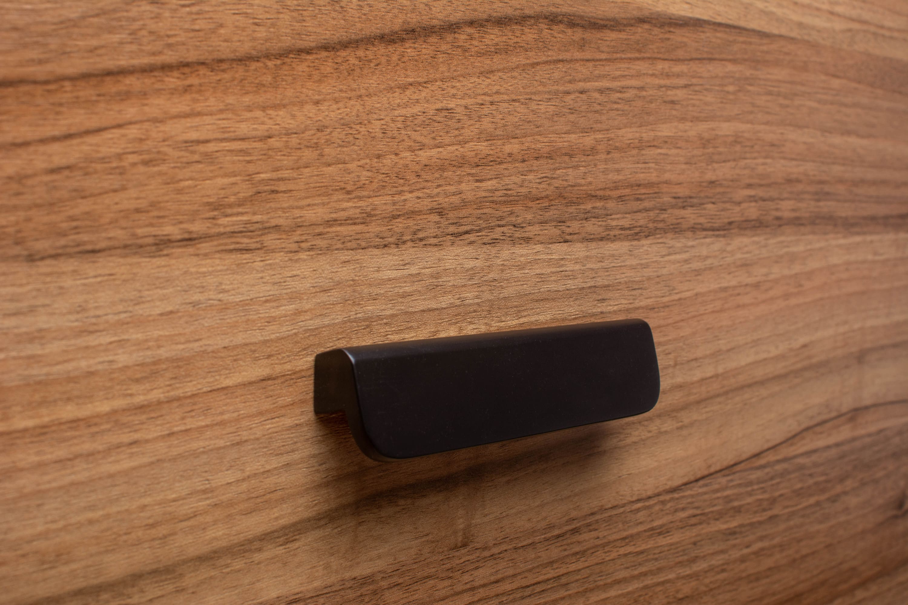 Stylish wide grip rounded black handle on walnut cabinet, combining functionality with modern aesthetics.