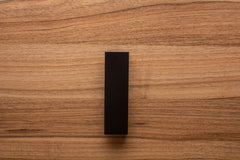 Wide grip black L-form handle on walnut cabinet, perfect for contemporary furniture design.