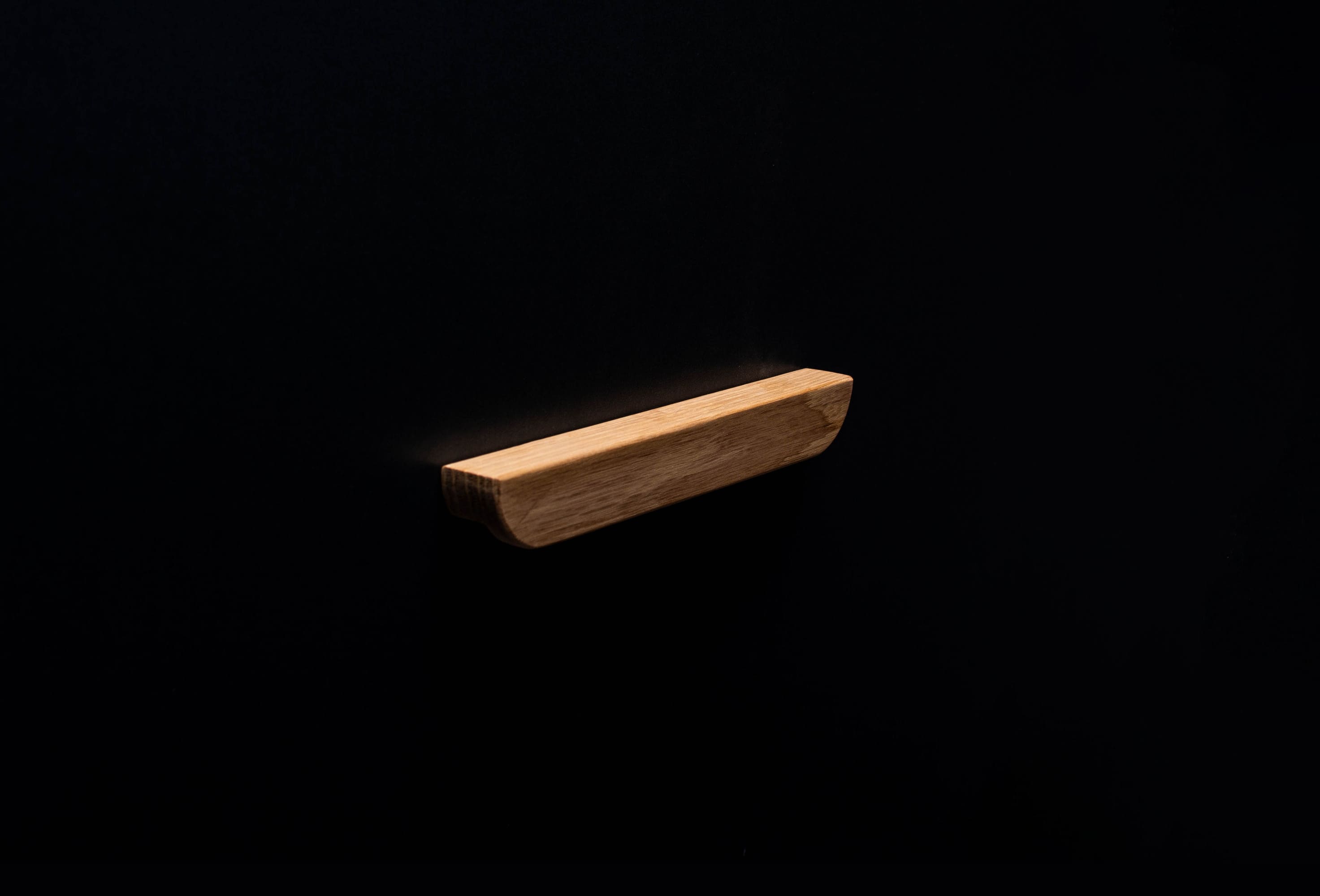 Raw oak drawer pull photographed against dark backdrop