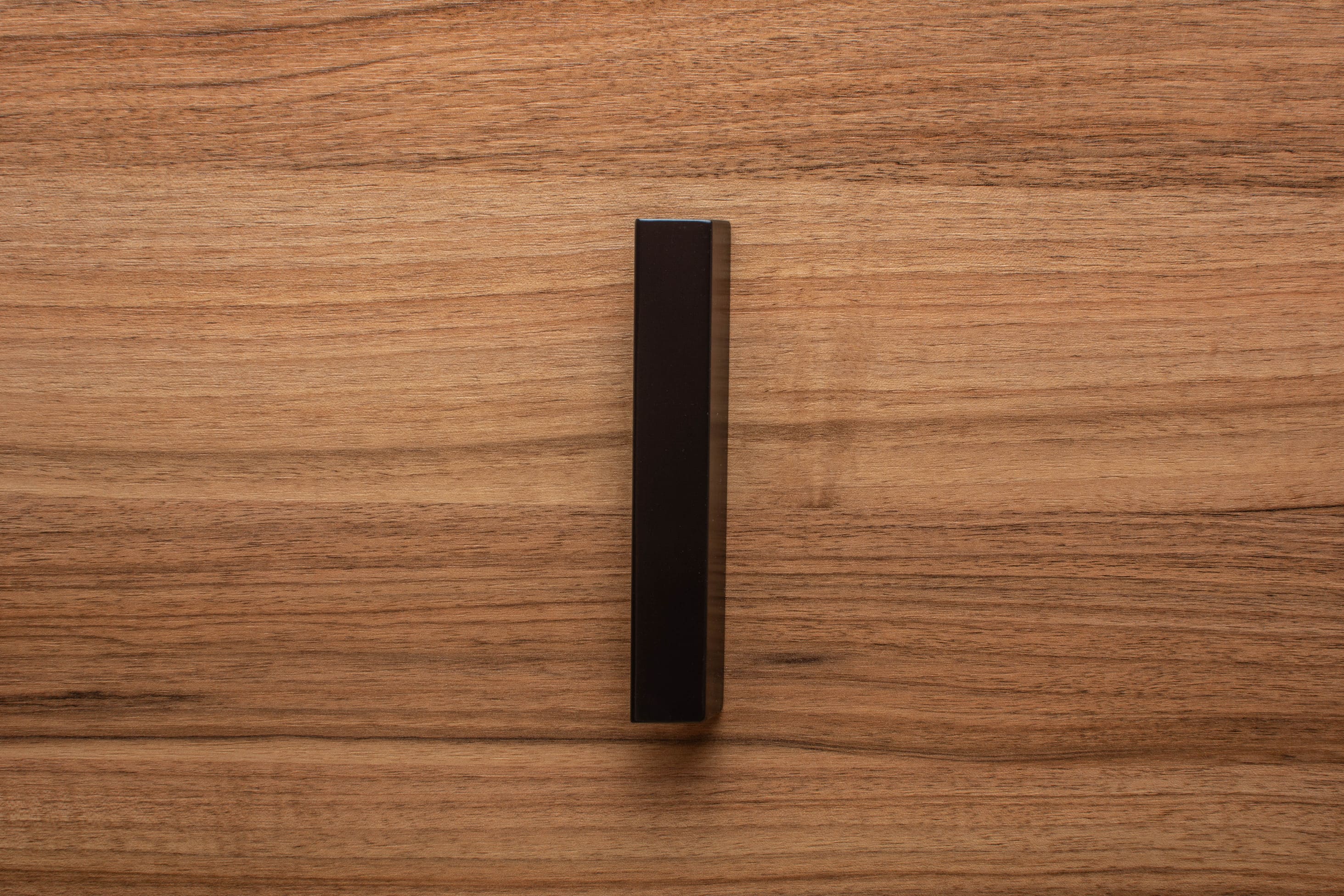 Angled view of black painted wooden handle on walnut cabinet, providing stylish contrast and depth.