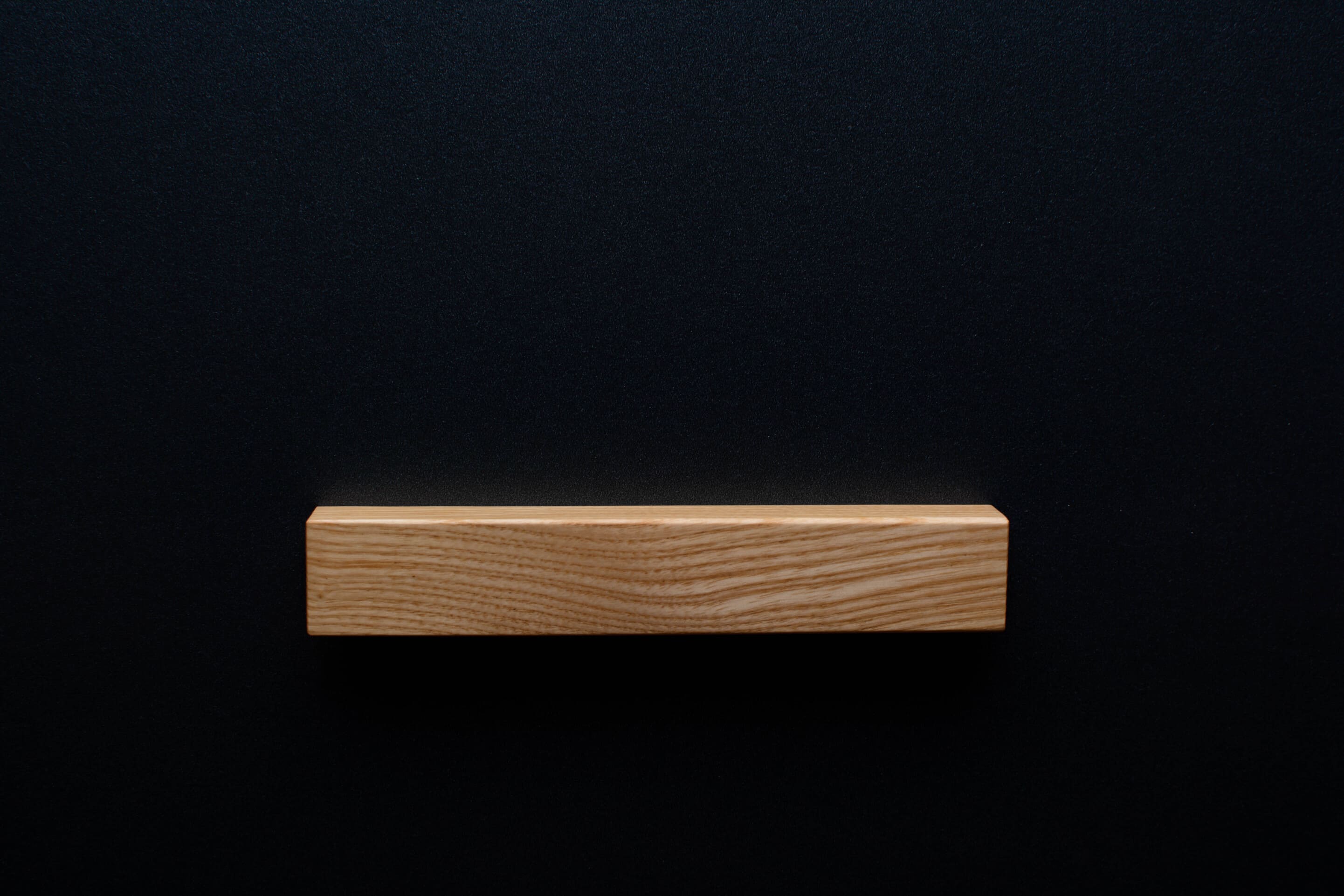 A detailed image of the Ash handle mounted on a black cabinet, capturing the texture of the wood and the stylish design from a wide perspective