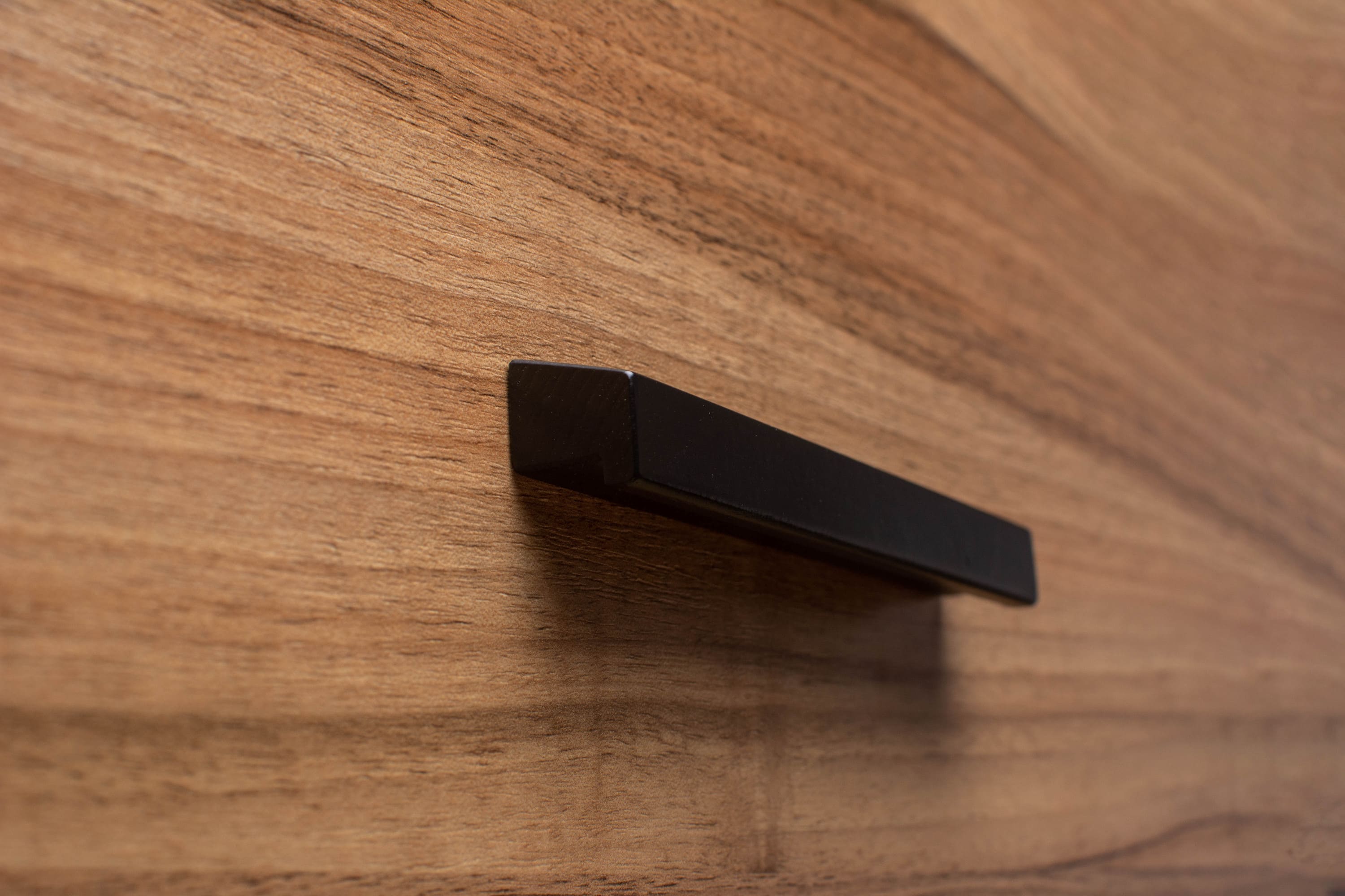 Sleek black painted wooden handle on walnut cabinet, combining modern style with natural wood grain.