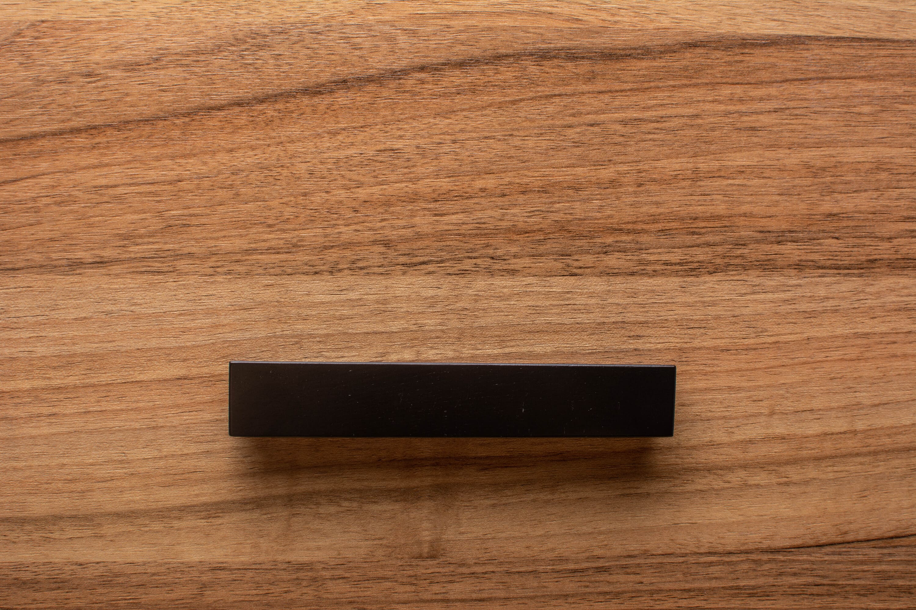 Bold black trapezoidal handle installed on walnut cabinet, enhancing contemporary style.