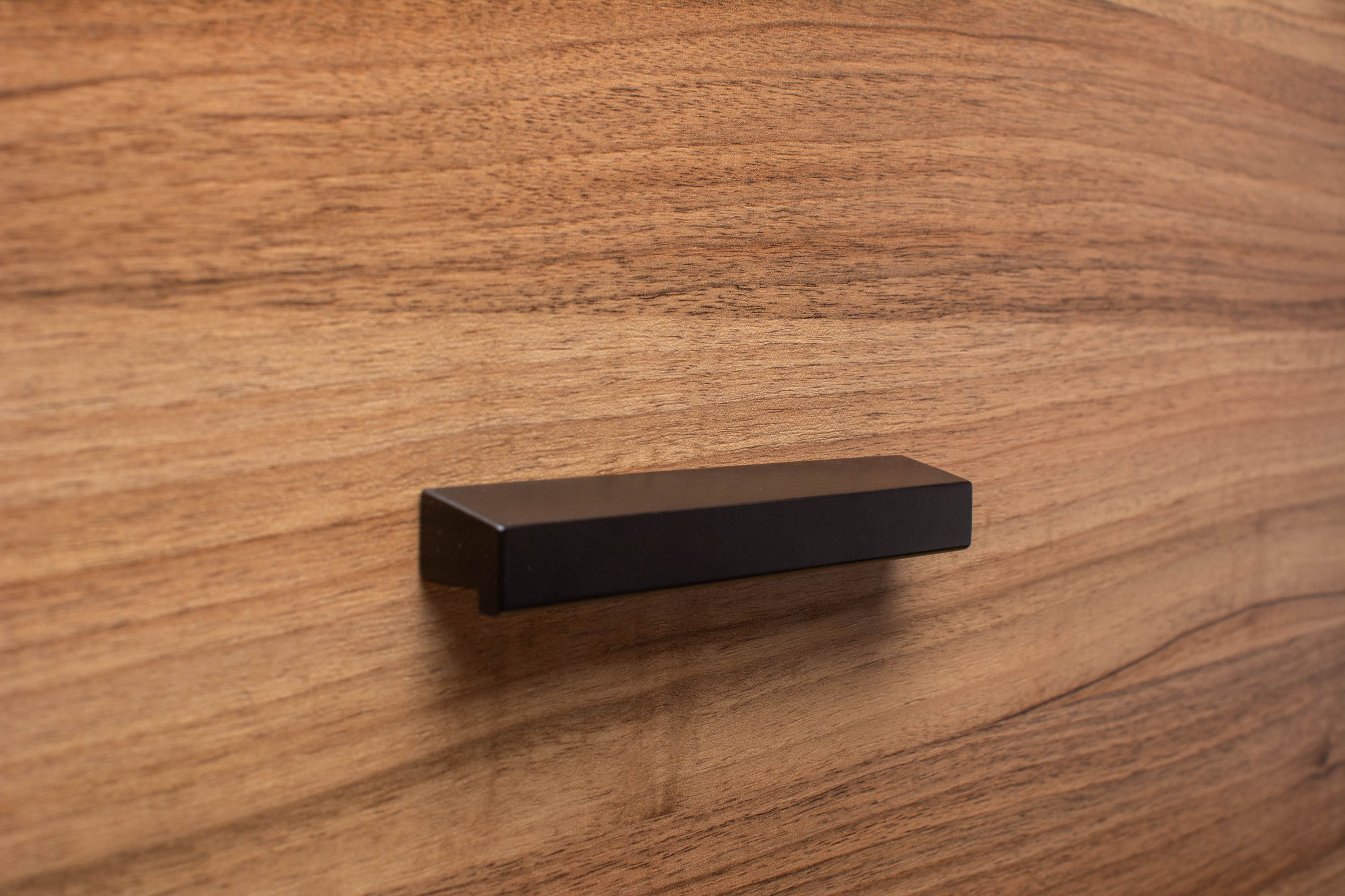 Black wooden cabinet handle in matte finish on walnut cabinet door, providing a bold contrast.