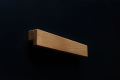 A close-up view of the sleek L-shaped Ash cabinet handle installed on a black cabinet, highlighting the contrast between the light wood and dark surface