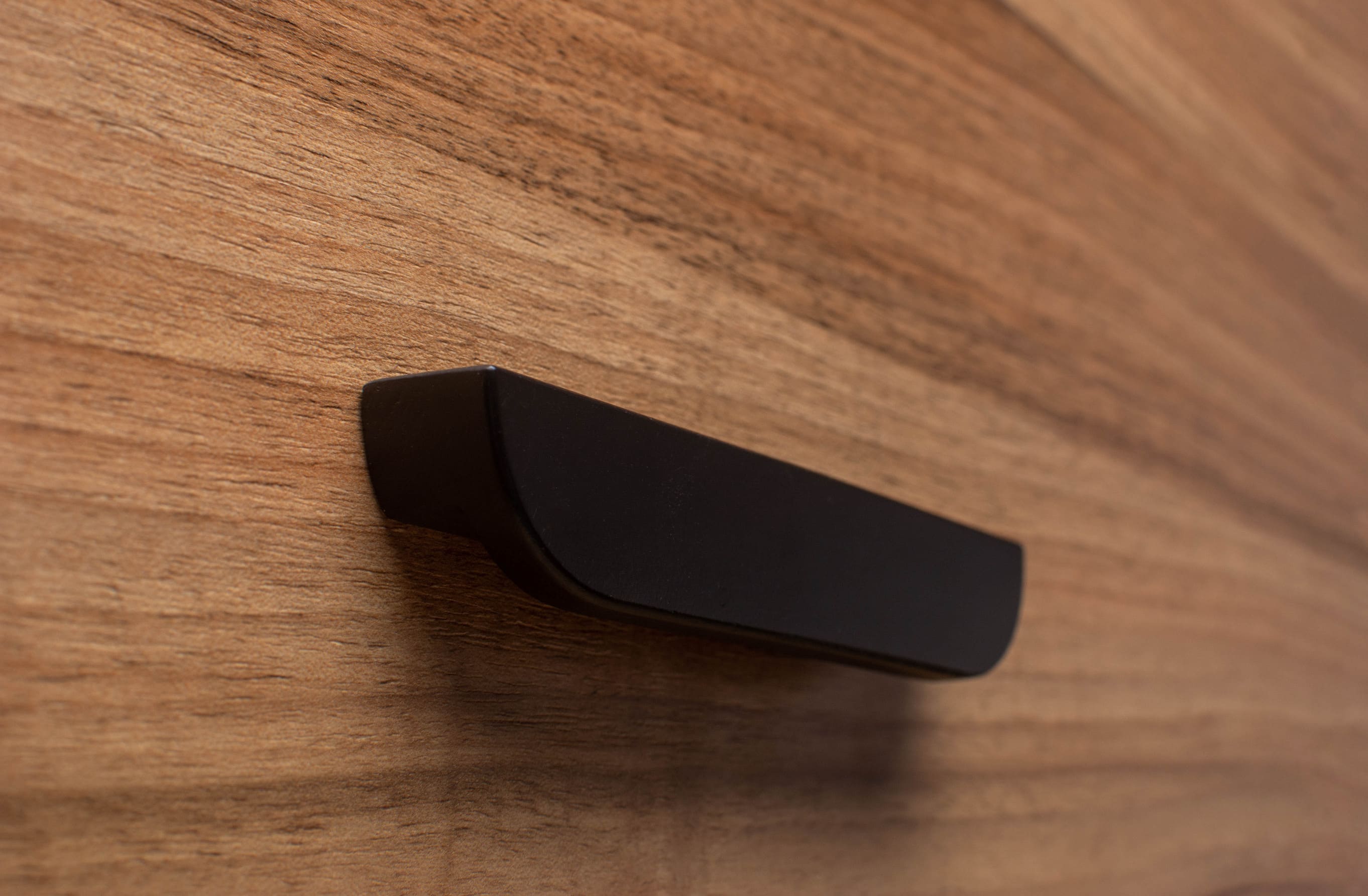 Matte black rounded handle on walnut cabinet, enhancing modern furniture with subtle curves.