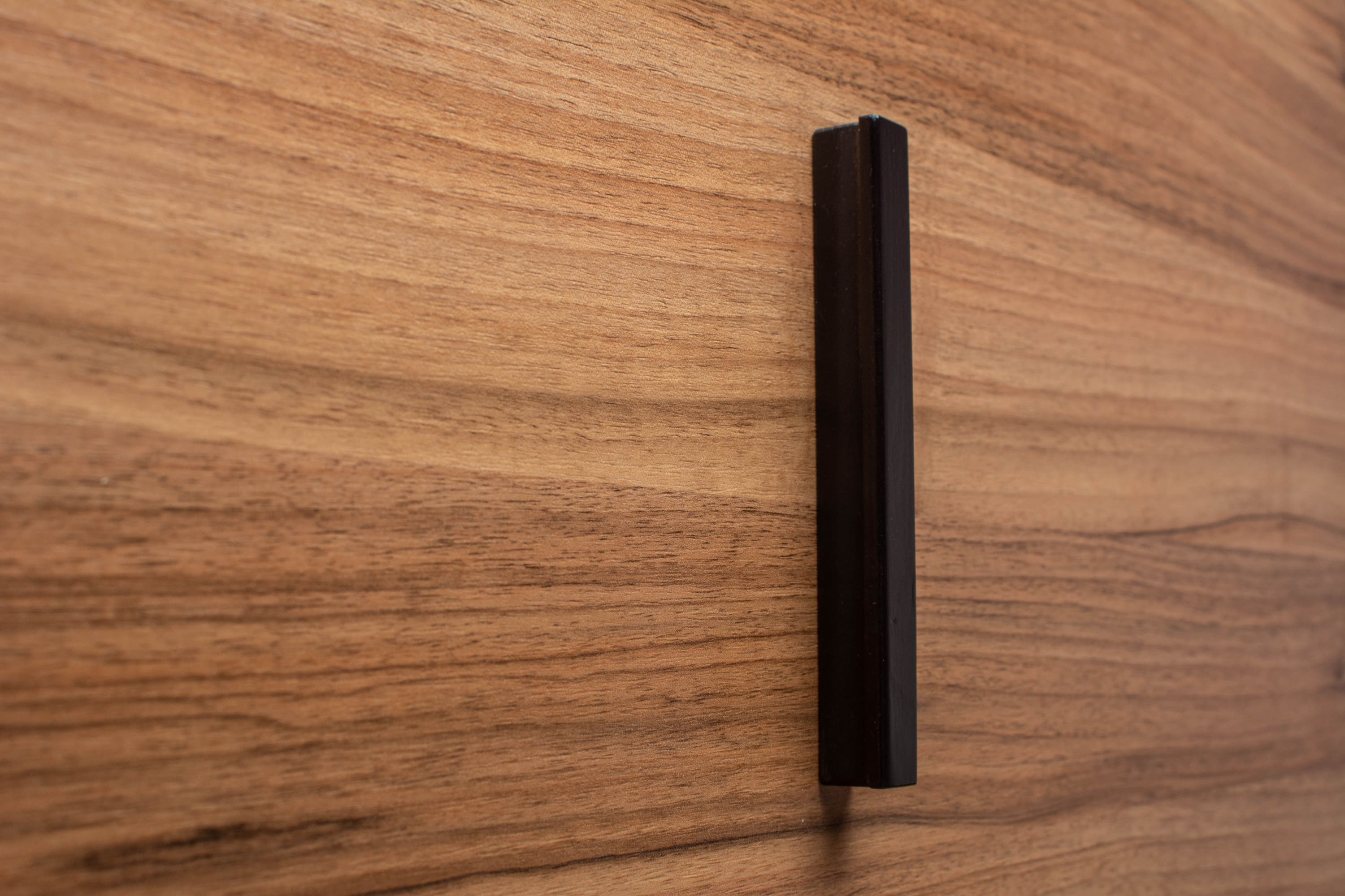 Front view of black painted handle installed on walnut wood, highlighting clean and modern design lines.