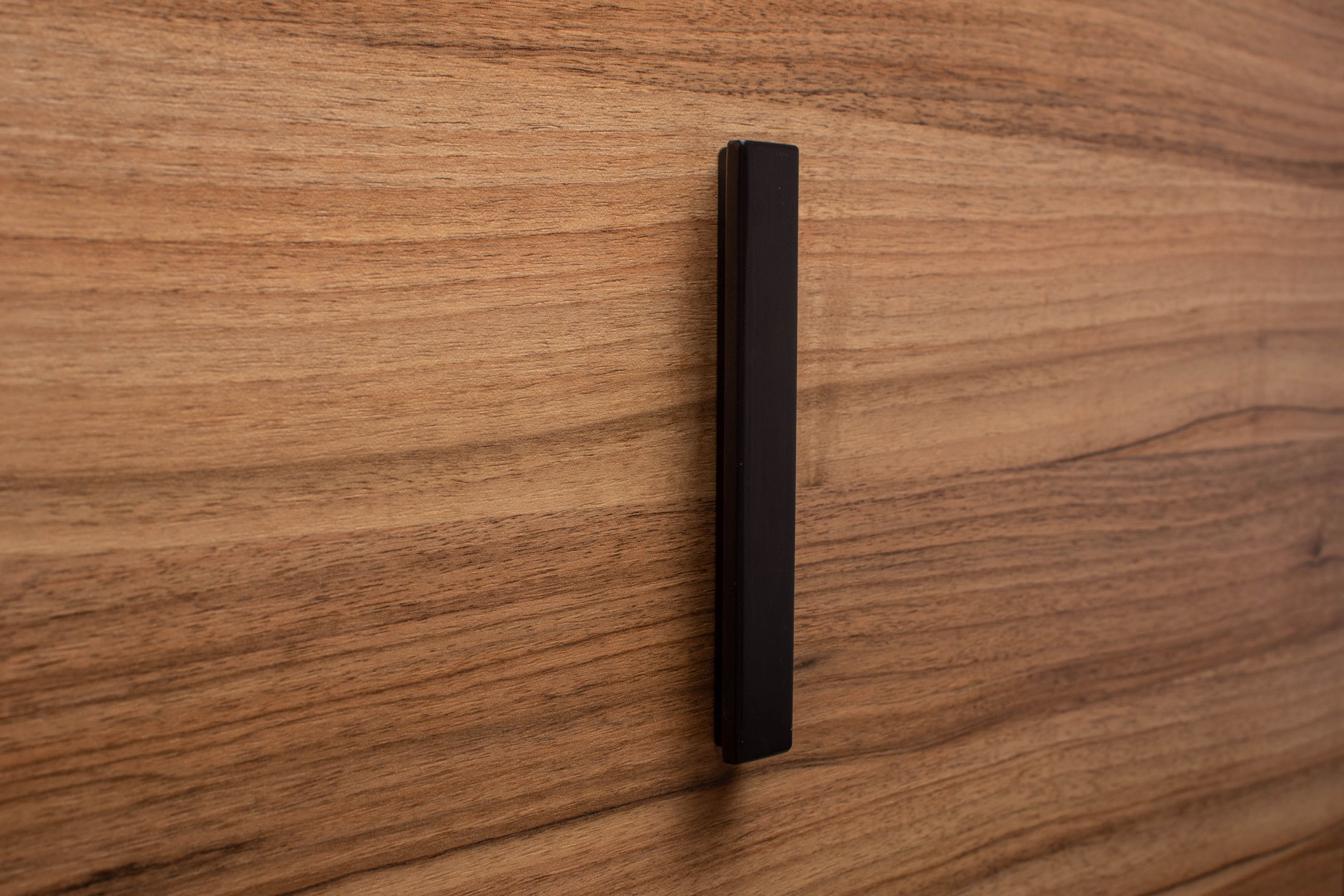 Black painted wooden handle attached to walnut drawer, showcasing modern elegance and clean lines.