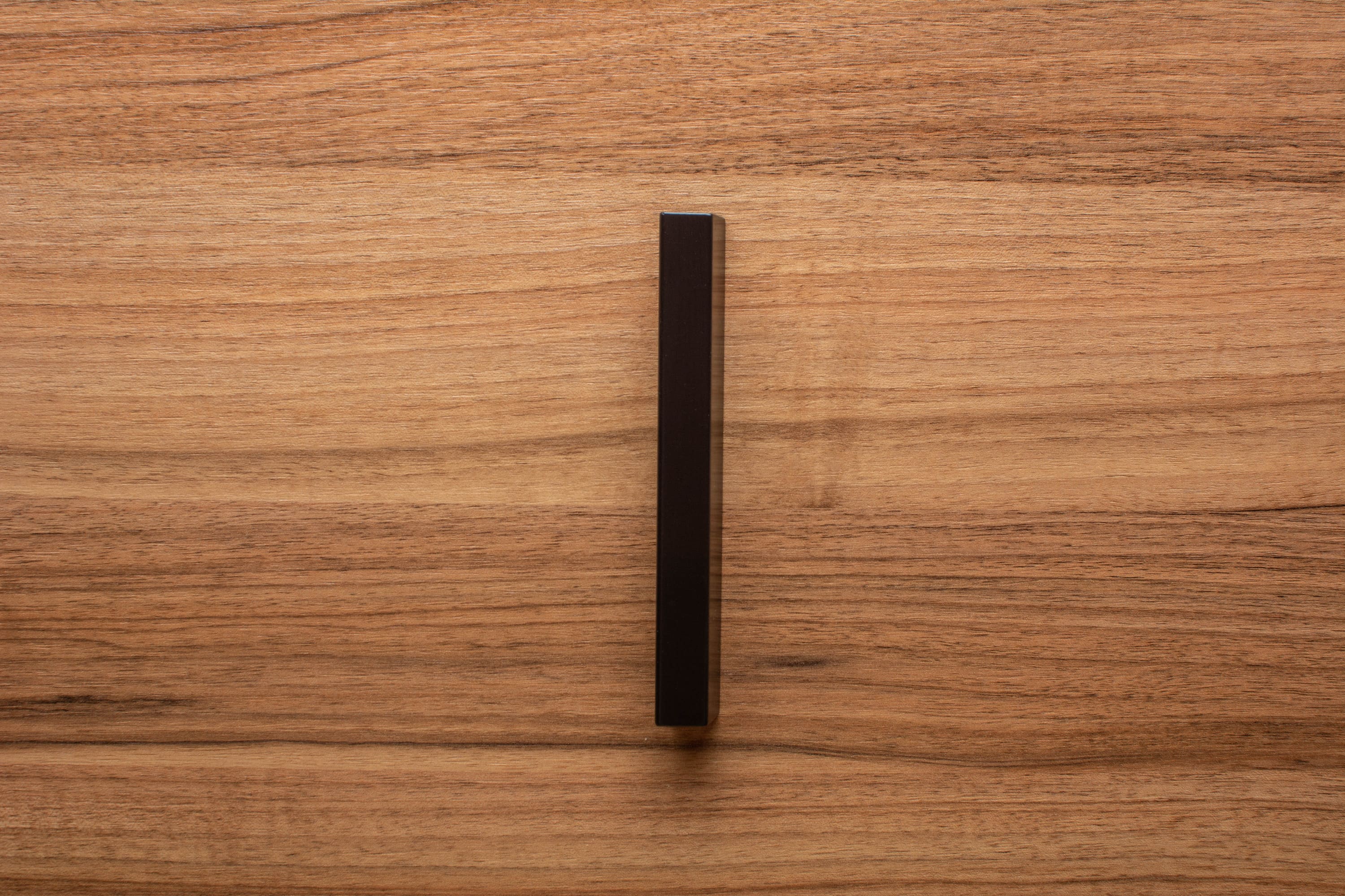 Detailed shot of black wooden handle mounted on walnut drawer, showcasing smooth finish and quality.