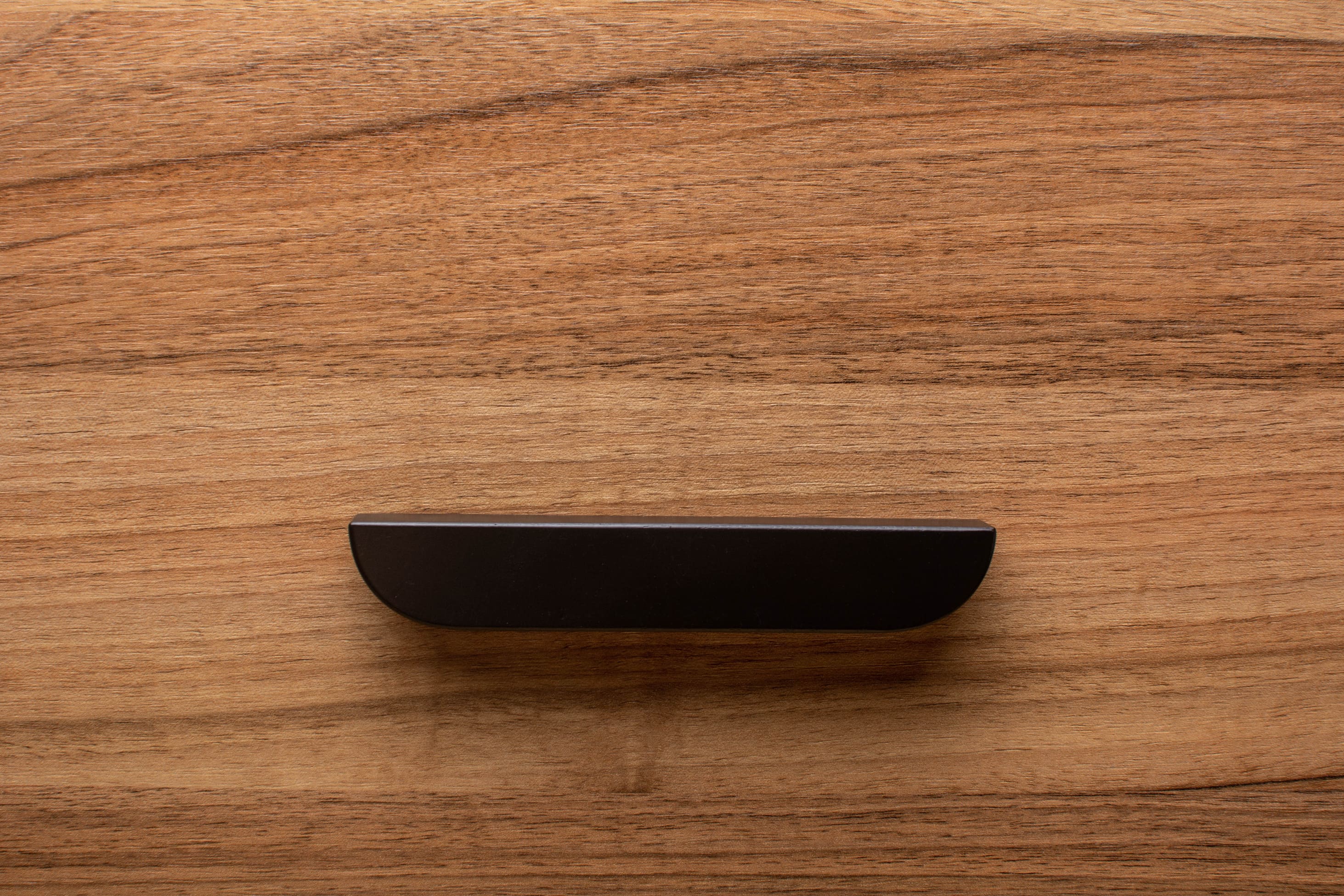 Rounded edge black handle on a walnut drawer, blending sleek design with timeless appeal.