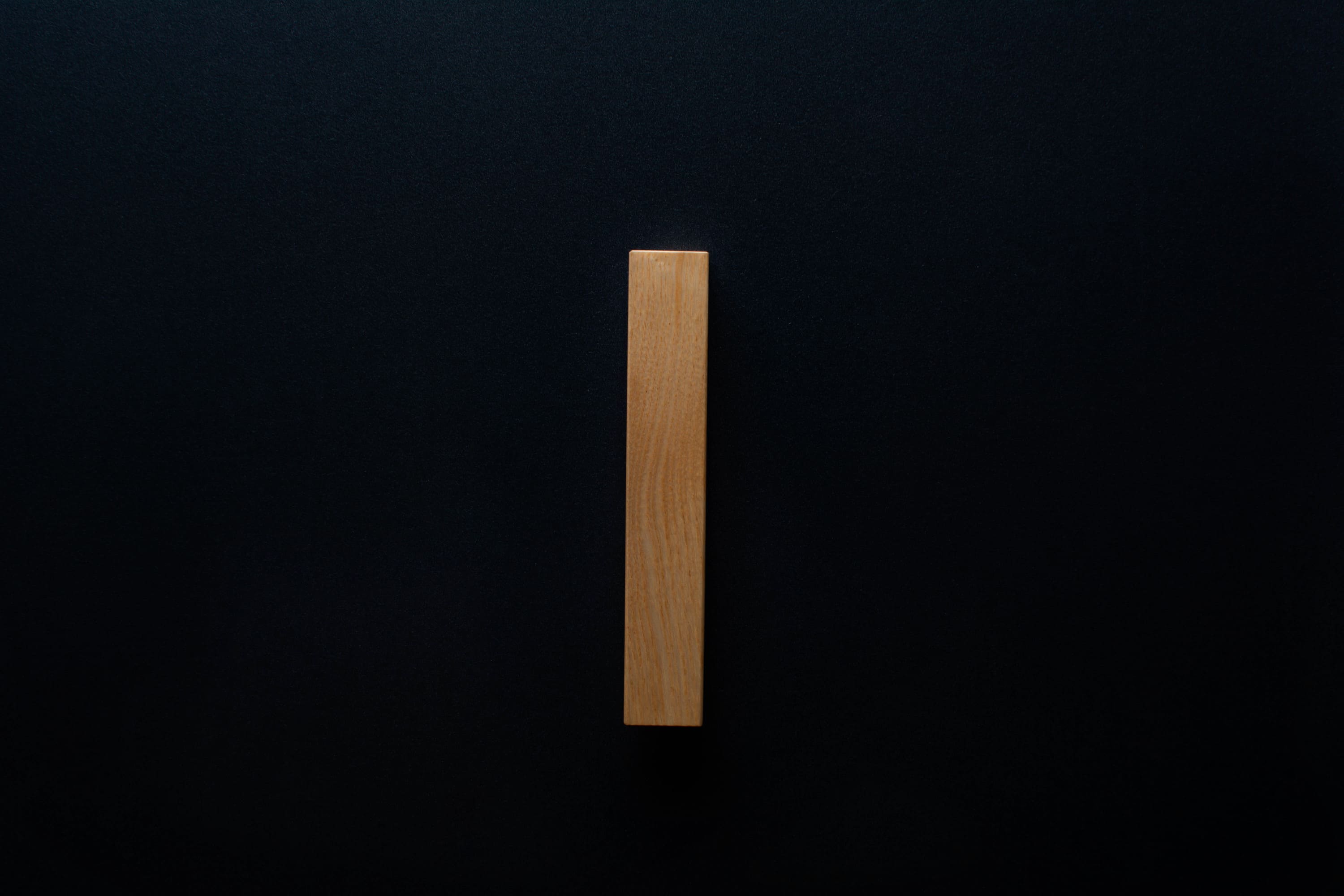 Side perspective of the L-shaped Ash handle mounted on a black cabinet, focusing on the smooth finish and elegant curve of the handle.