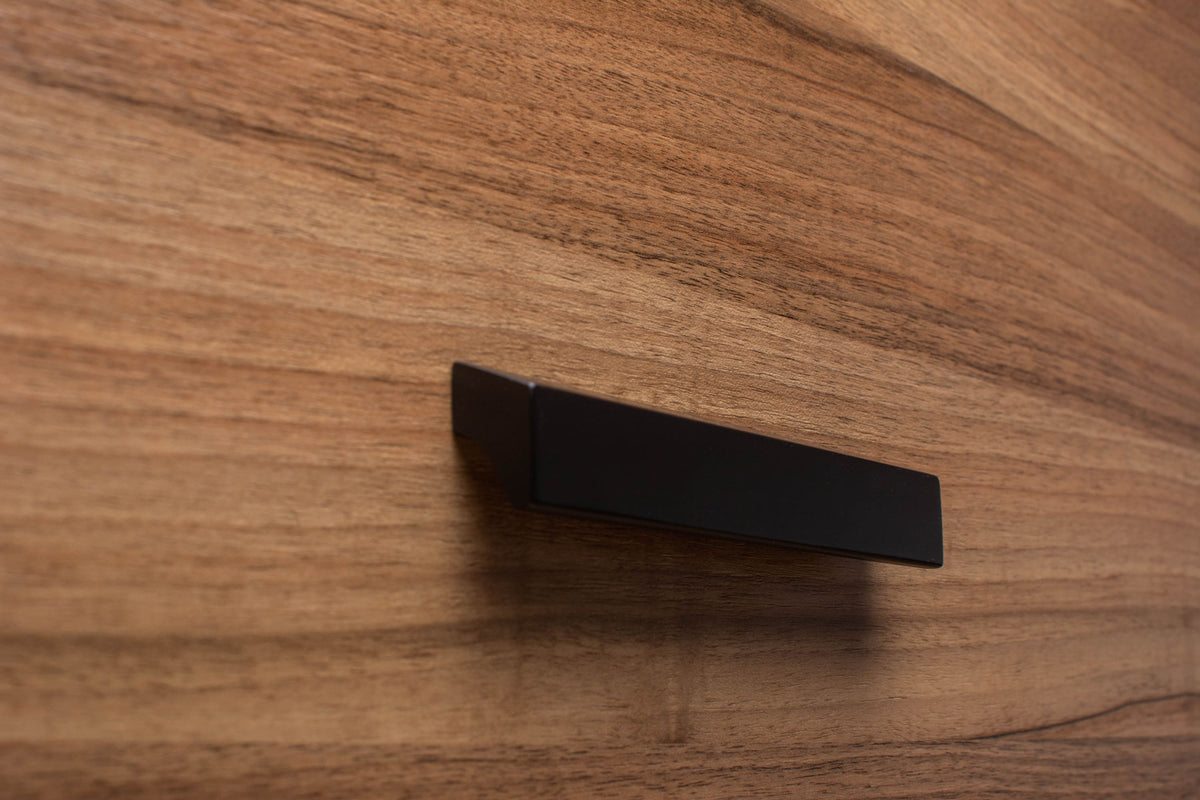 Close-up of sleek black wooden handle on walnut cabinet, showcasing fine craftsmanship and texture.