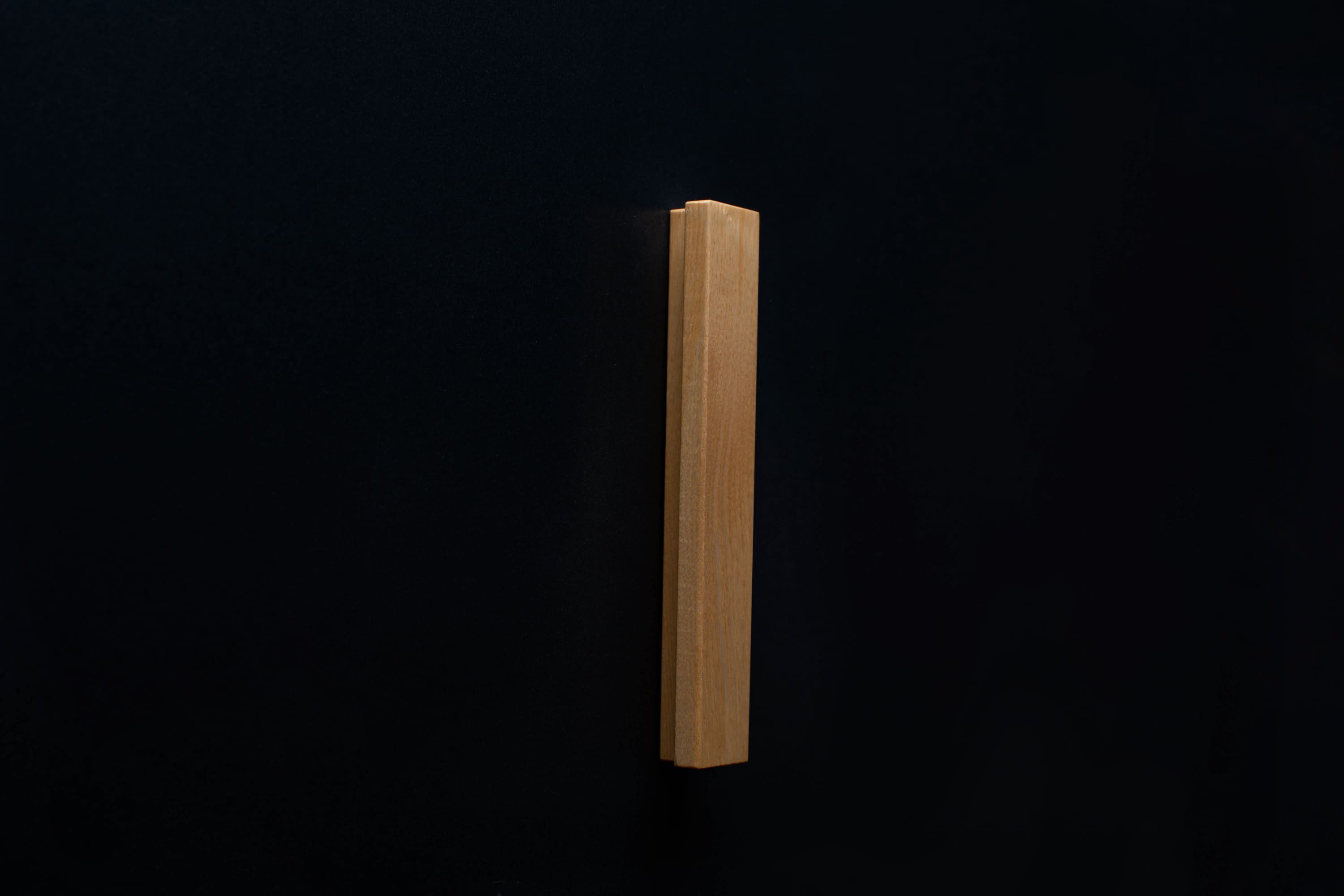 A top-down view of the modern Ash handle affixed to a black cabinet, highlighting the sleek shape and how it complements the dark furniture.